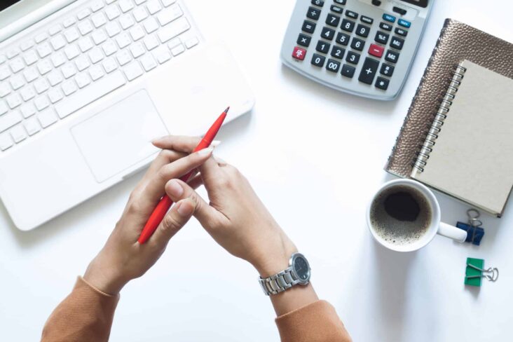 mulher com portatil calculadora blocos de notas e chavena de cafe em cima da mesa branca