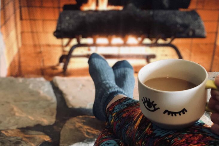 pessoa deitada a lareira com chavena nas pernas