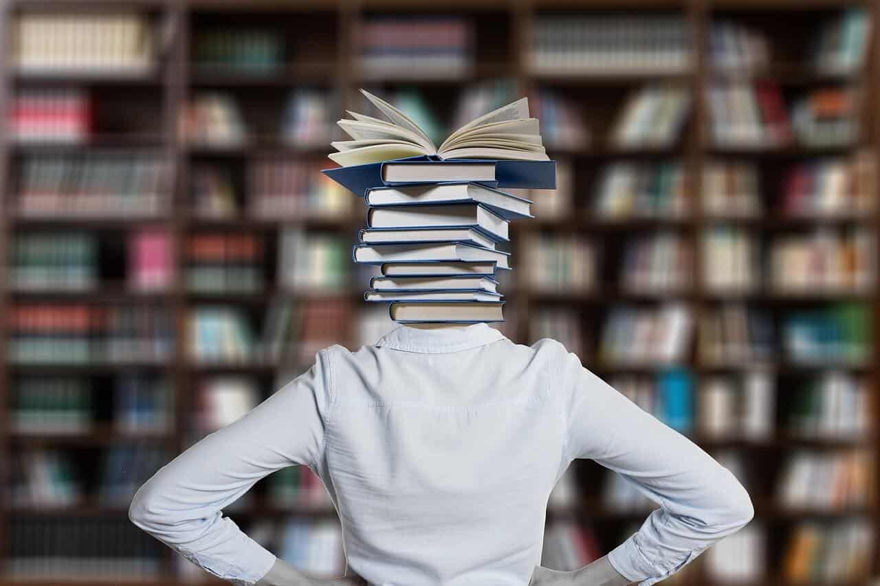 jovem mulher, numa biblioteca, de costas com a cabeça substituída por uma pilhade de livros