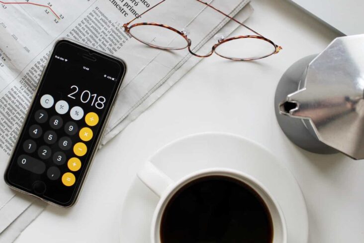 jornais abertos com calculadora em cima e chãvens de café