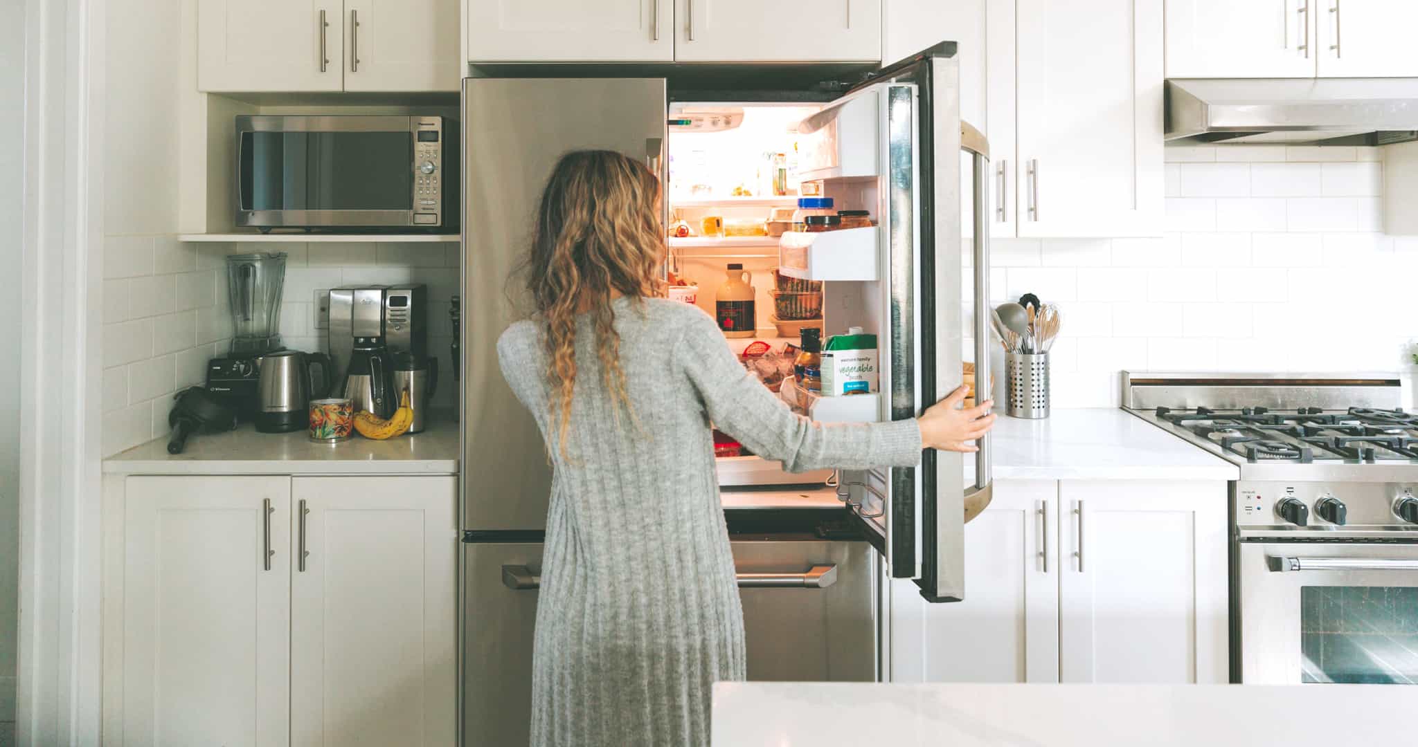 Mulher na cozinha com a porta do frigorífico aberta