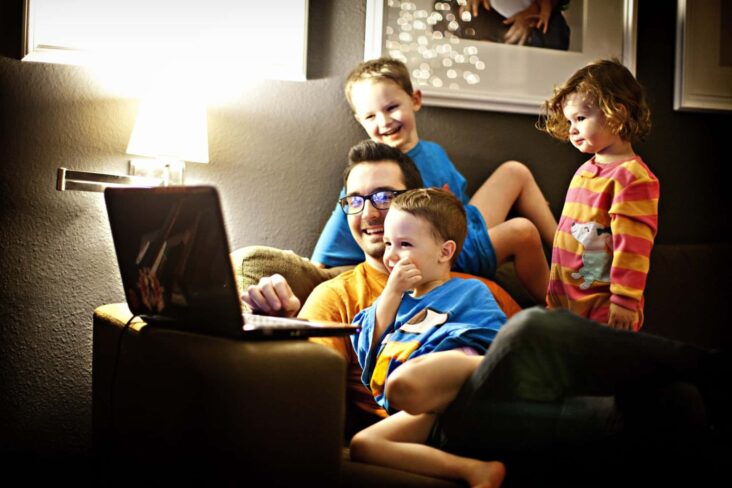 Pai com três filhos no sofá a ver o computador