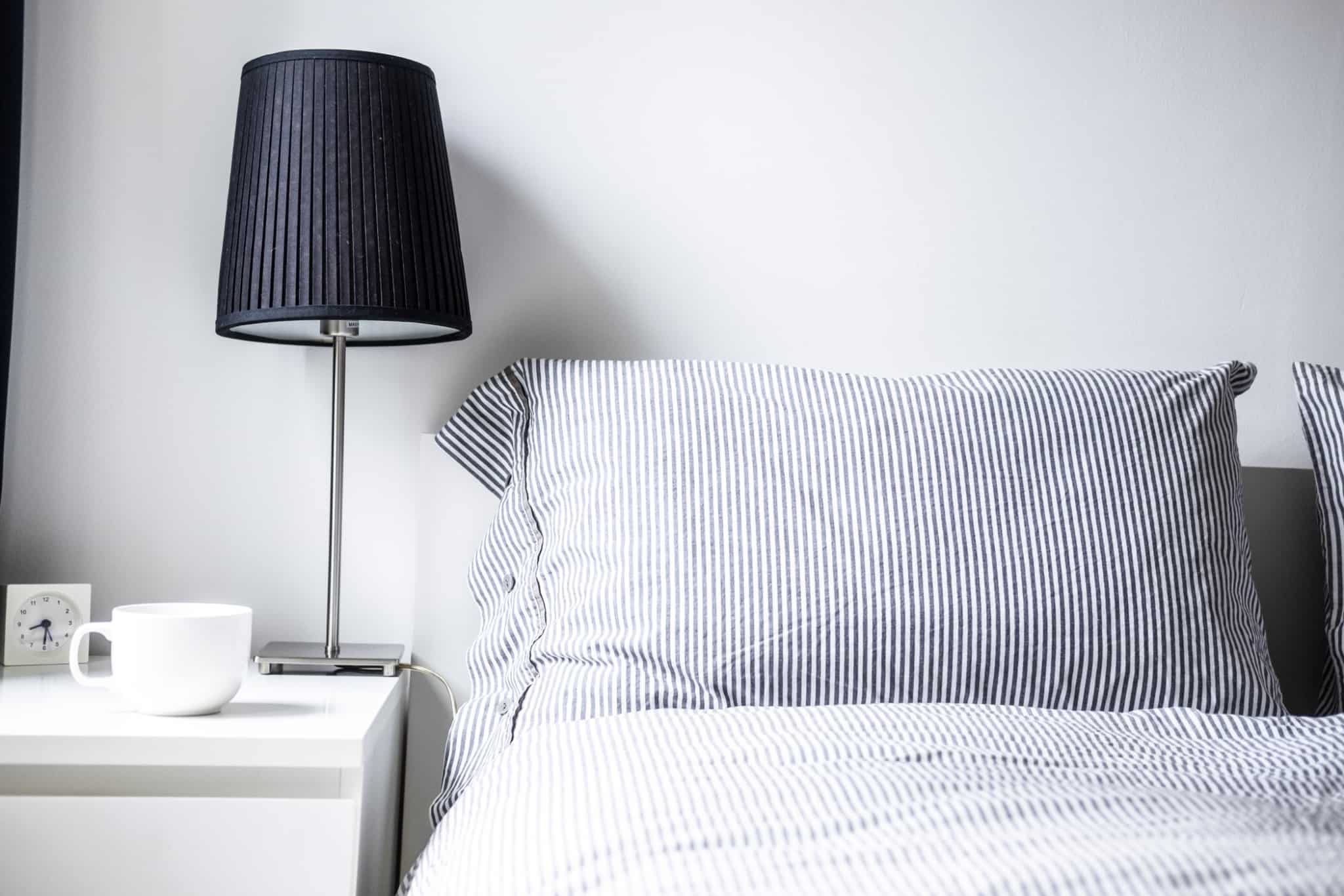 lampada de quarto em cima de uma mesa de cabeceira e com a cama ao lado