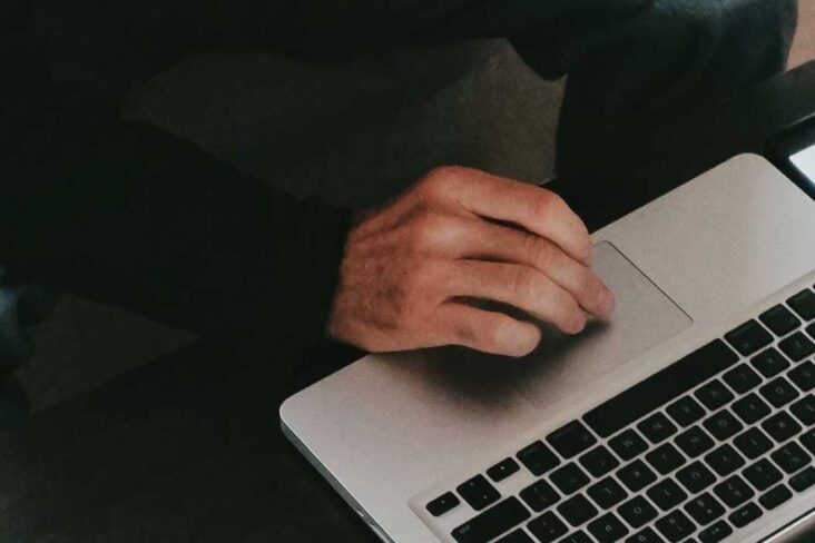 Homem em frente ao computador e com um bloco e uma caneta ao seu lado.