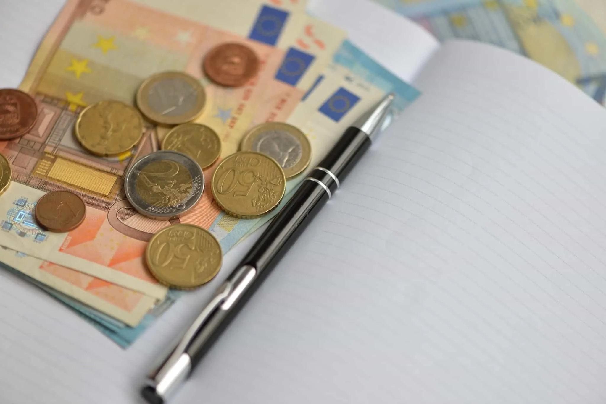 Notas e moedas de euro ao lado de um caneta