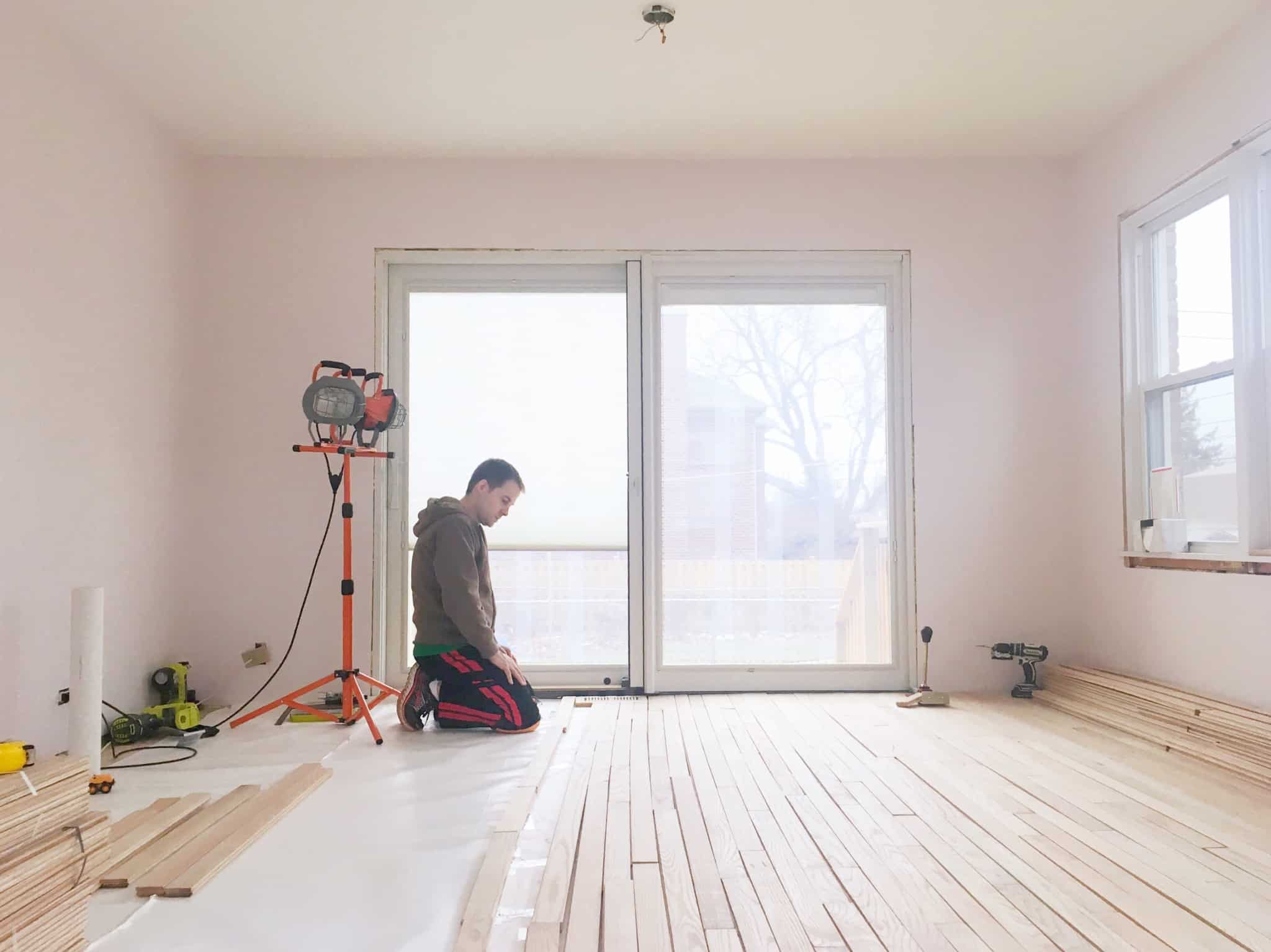 Vou fazer obras de melhoramento, preciso da autorização do condomínio? Homem ajoelhado no chão a aplicar soalho numa casa