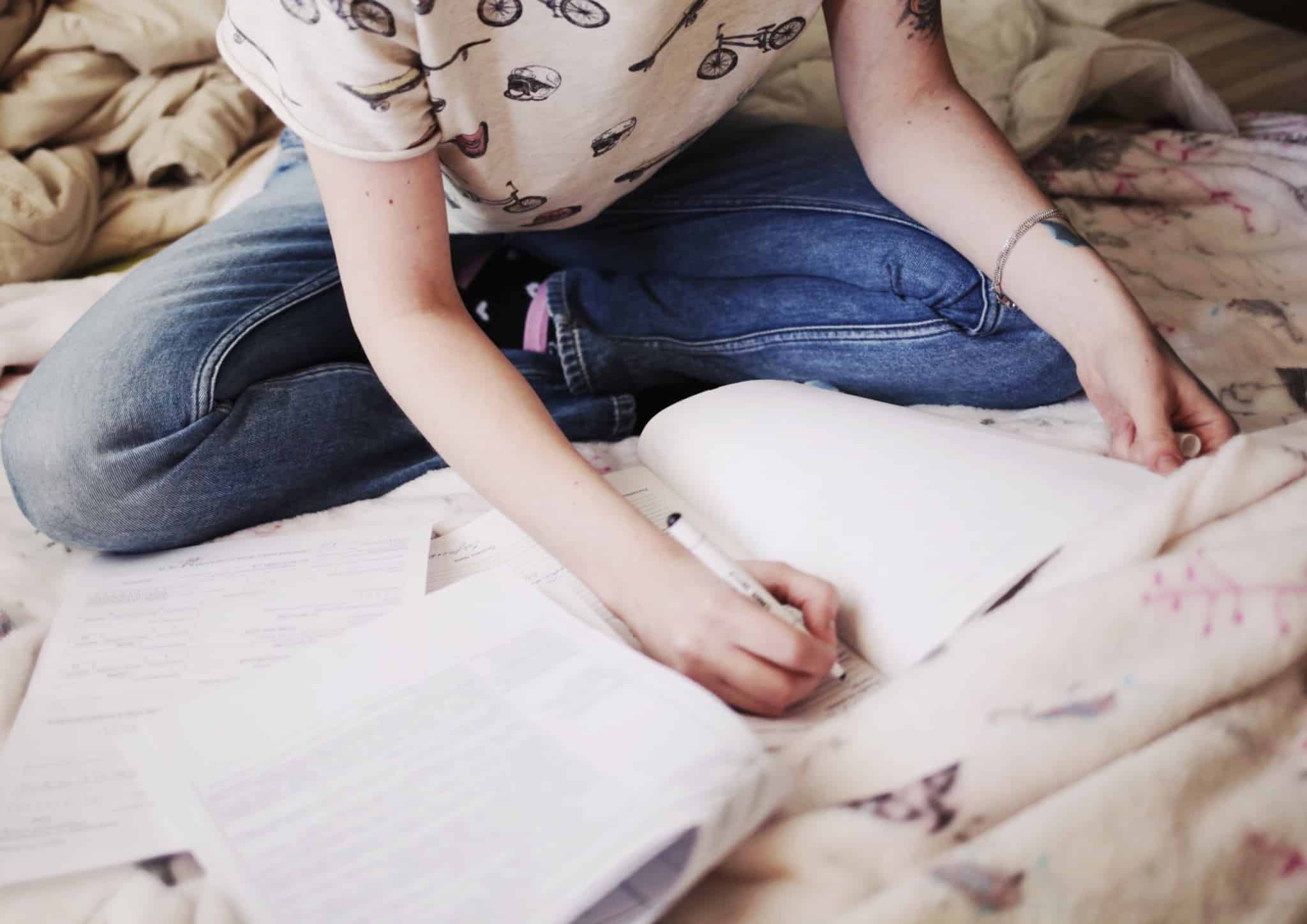 rapariga sentada em cima da cama a escrever em papel