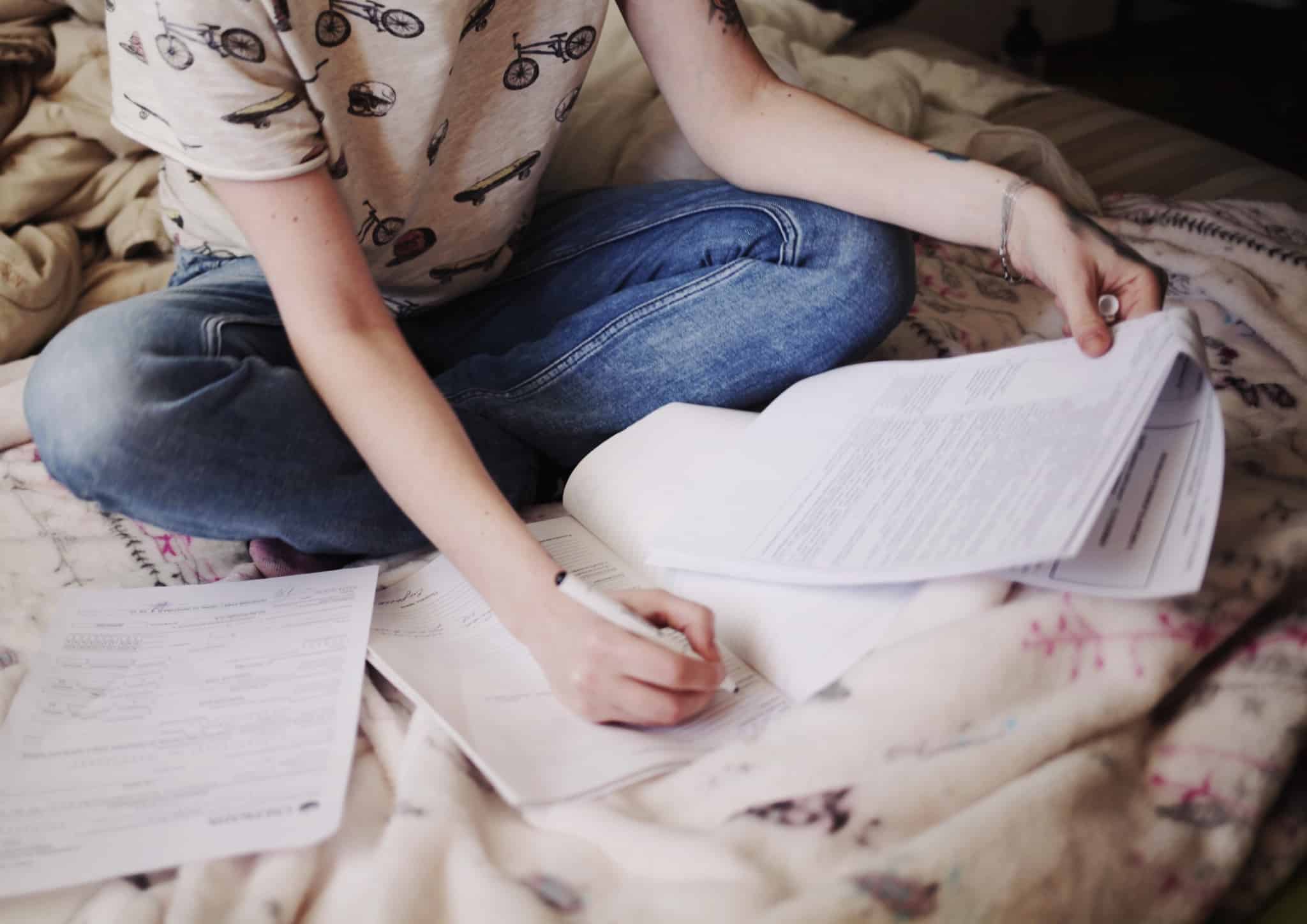 rapariga sentada na cama a escrever num papel