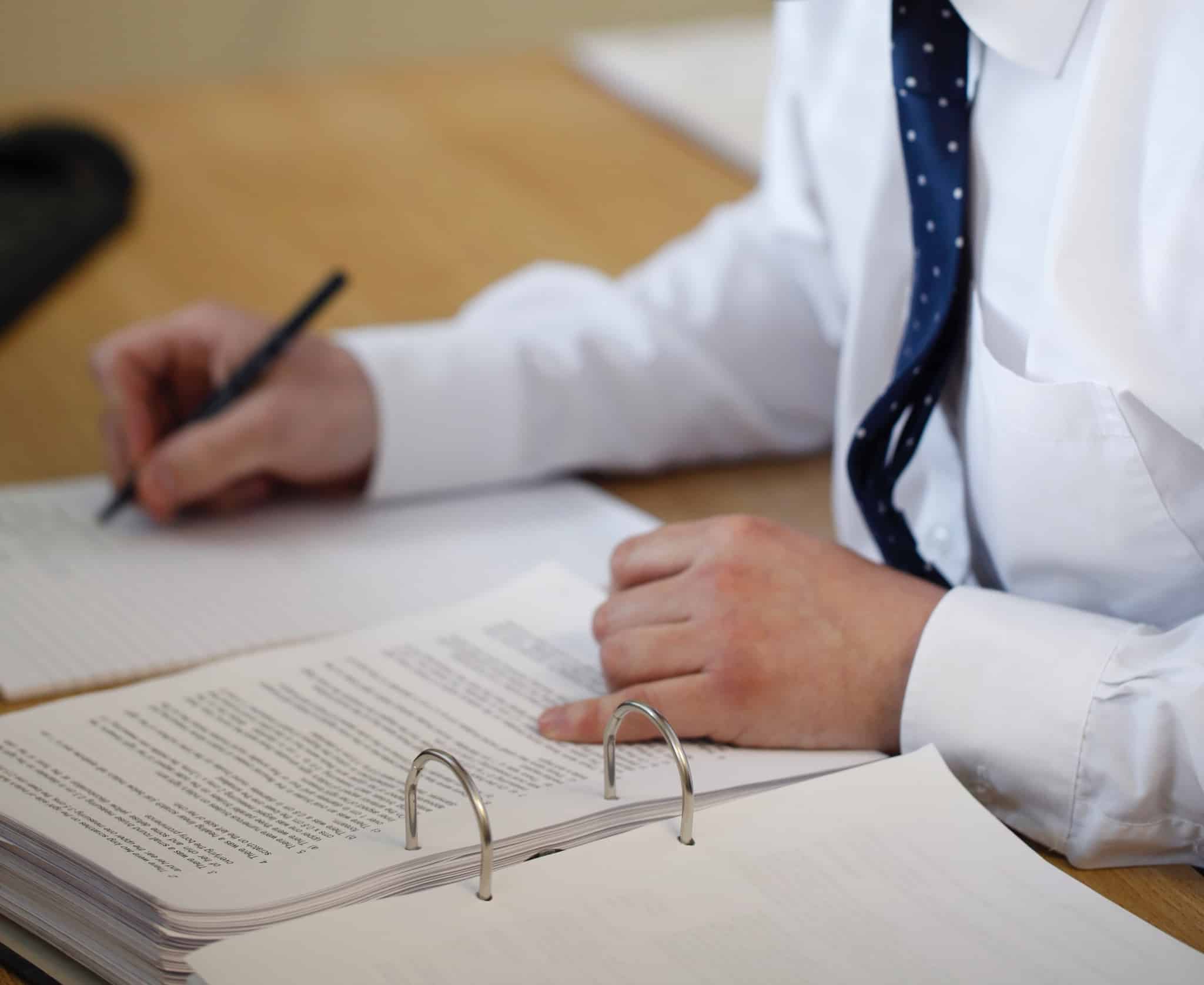 pessoa com gravata a escrever uma folha com um dossier aberto