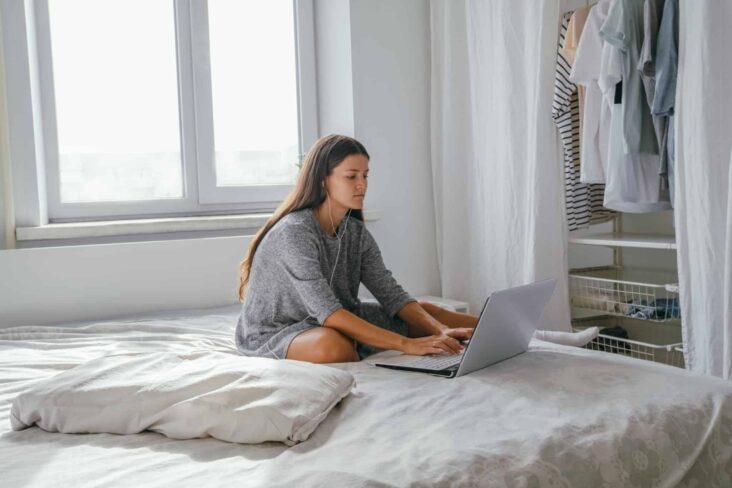 rapariga sentada na cama a escrever no computador