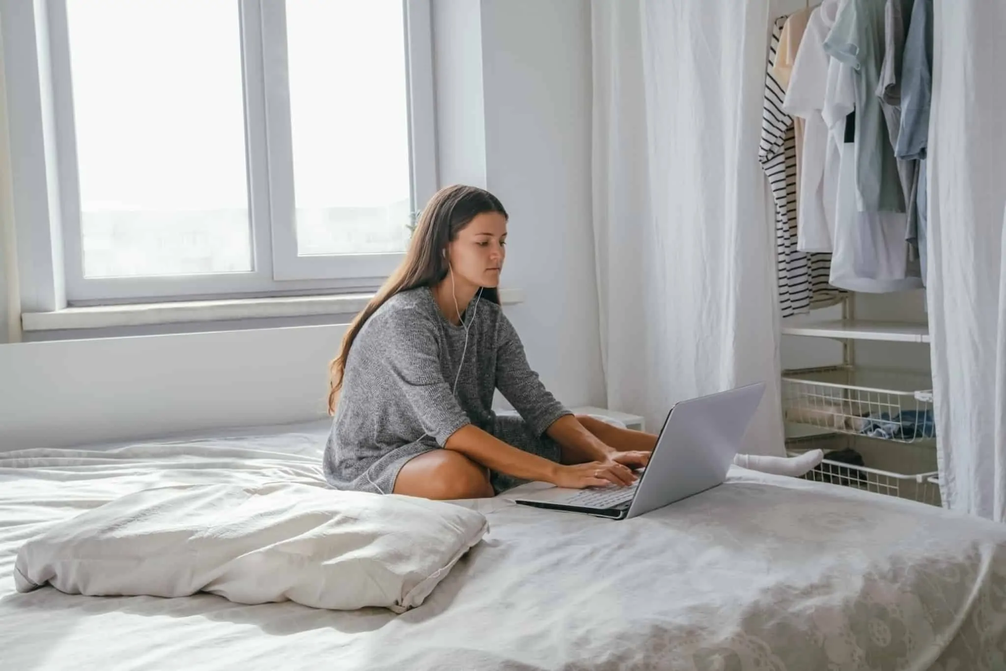 Trabalho remoto: uma tendência que veio para ficar? rapariga sentada na cama a escrever no computador