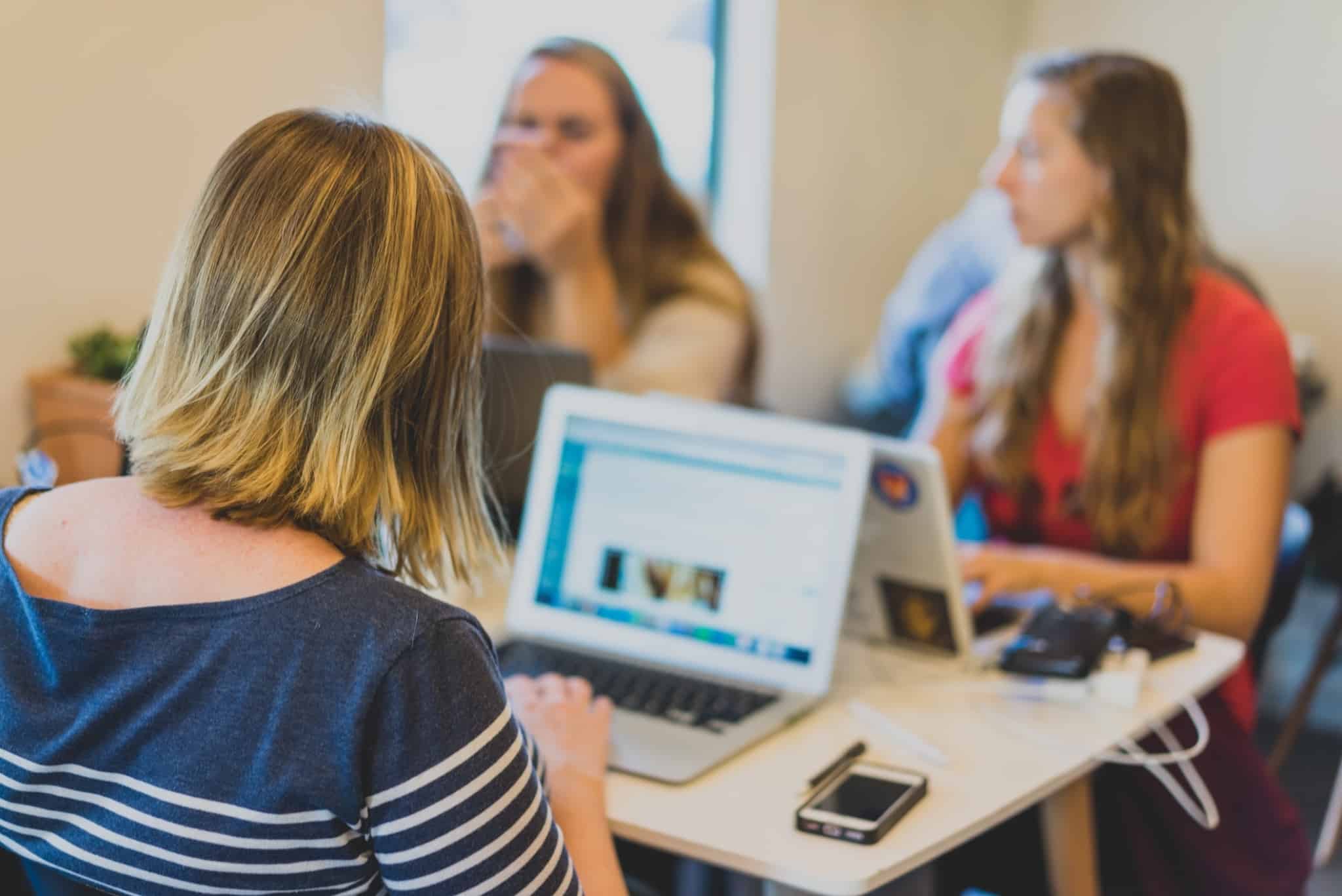 três raparigas a mexer nos portáteis em cima da mesa