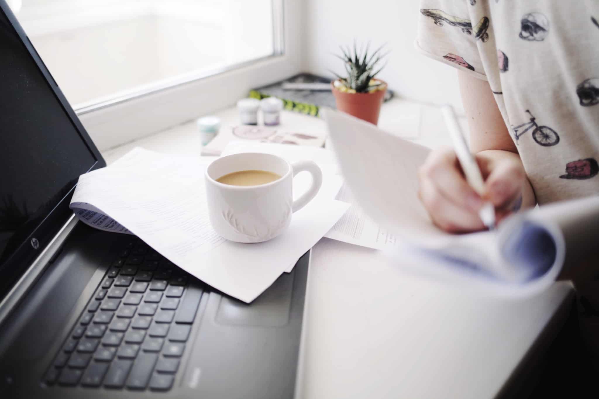 rapariga com uma chavena de cafe ao lado a escrever no bloco