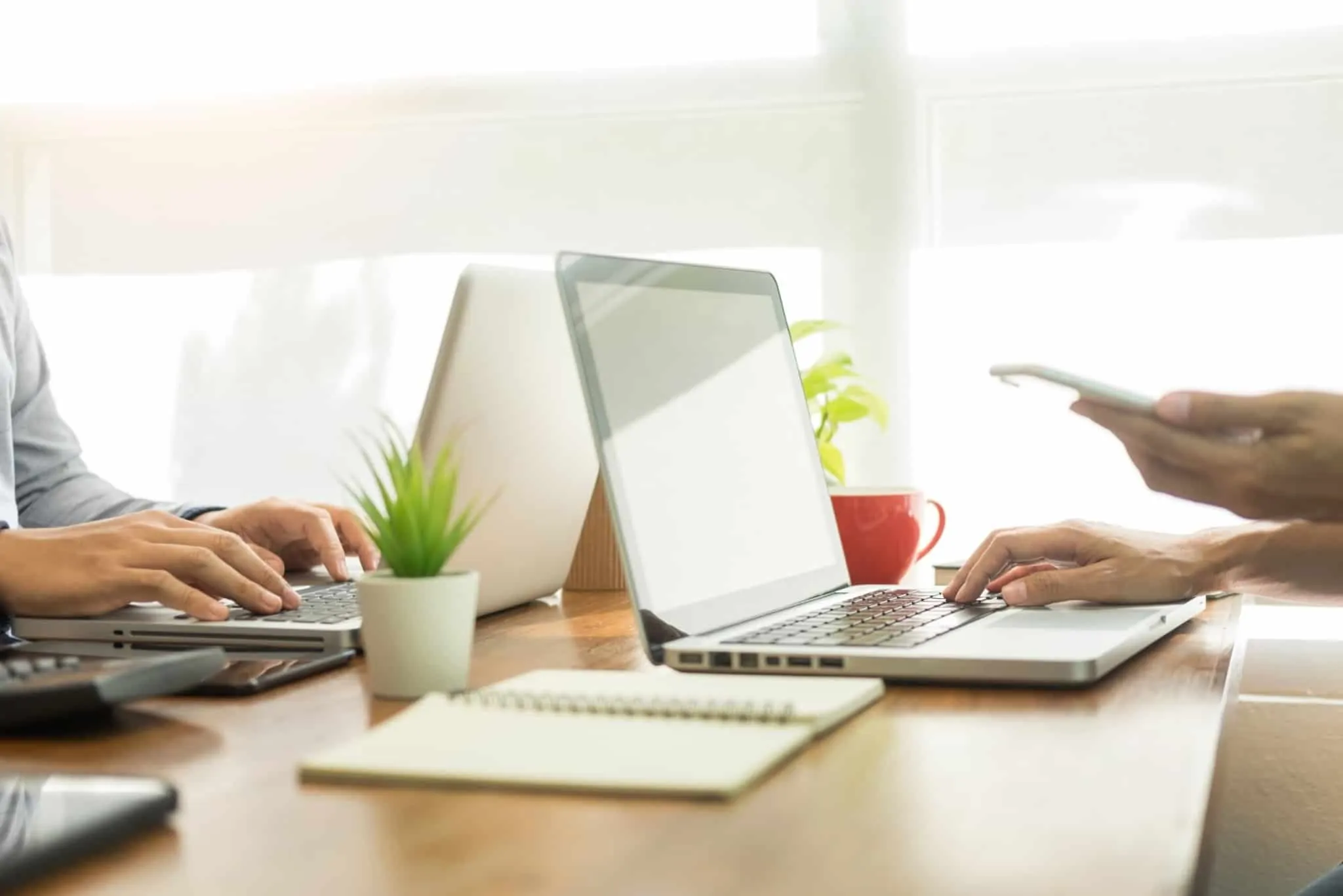 Precisa de cancelar uma transferência? Saiba como proceder dois computadores e pessoa a agarrar telemóvel