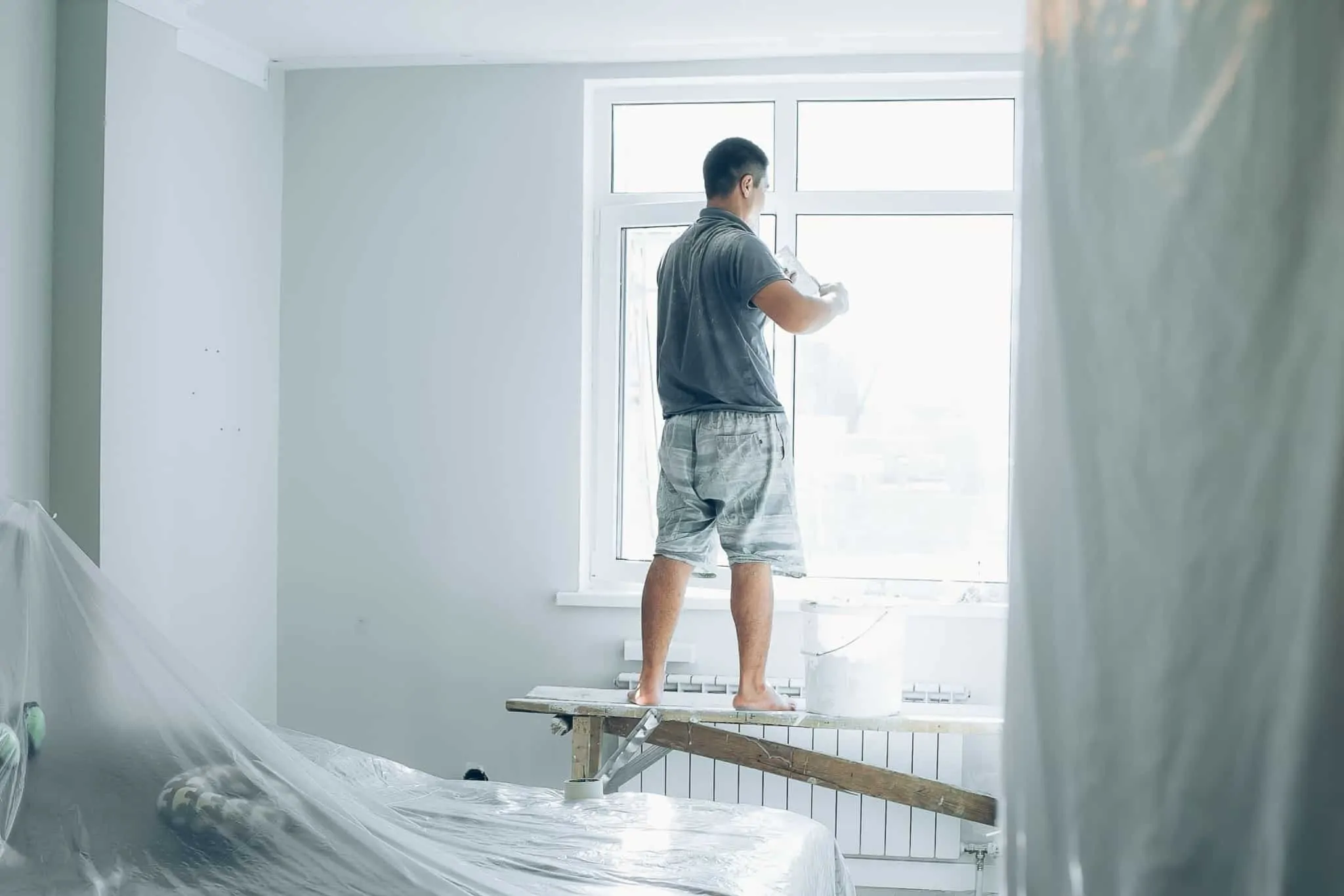 Saiba como ter ajuda do Estado para tornar a sua casa mais sustentável Homem está a pintar o interior de uma casa, junto a uma janela