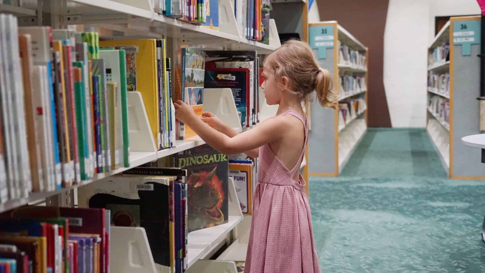 rapariga loira na biblioteca a ver livros