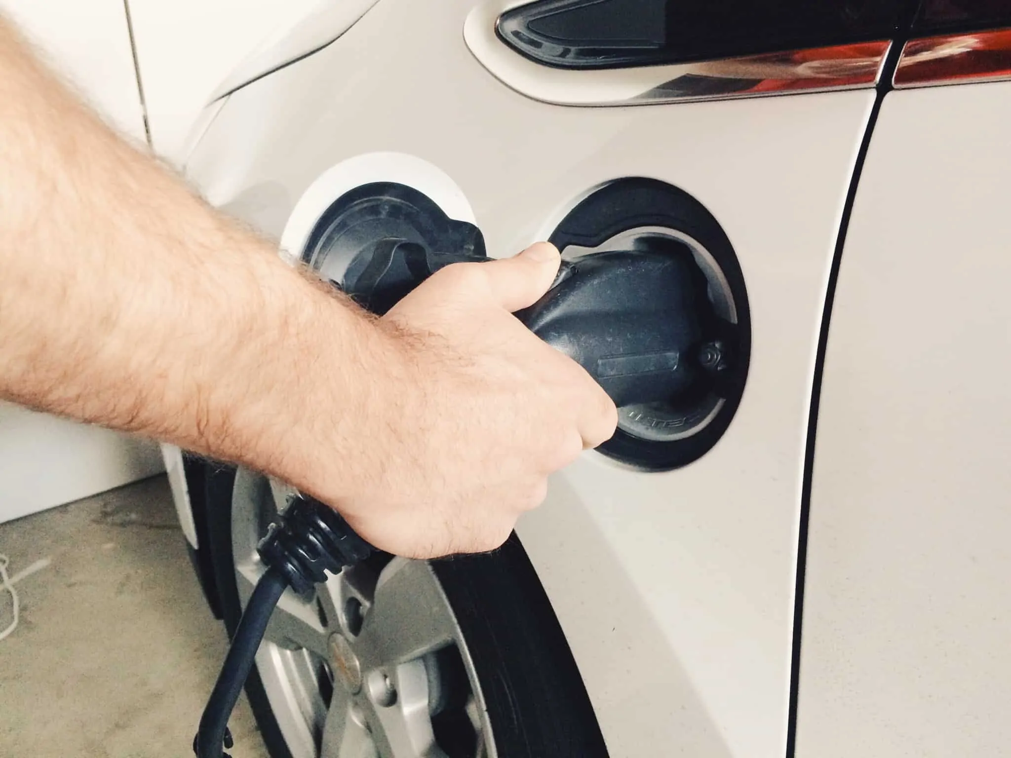 Fiscalidade Verde: metas, benefícios e penalizações Mão de um homem a pôr o carro elétrico a carregar