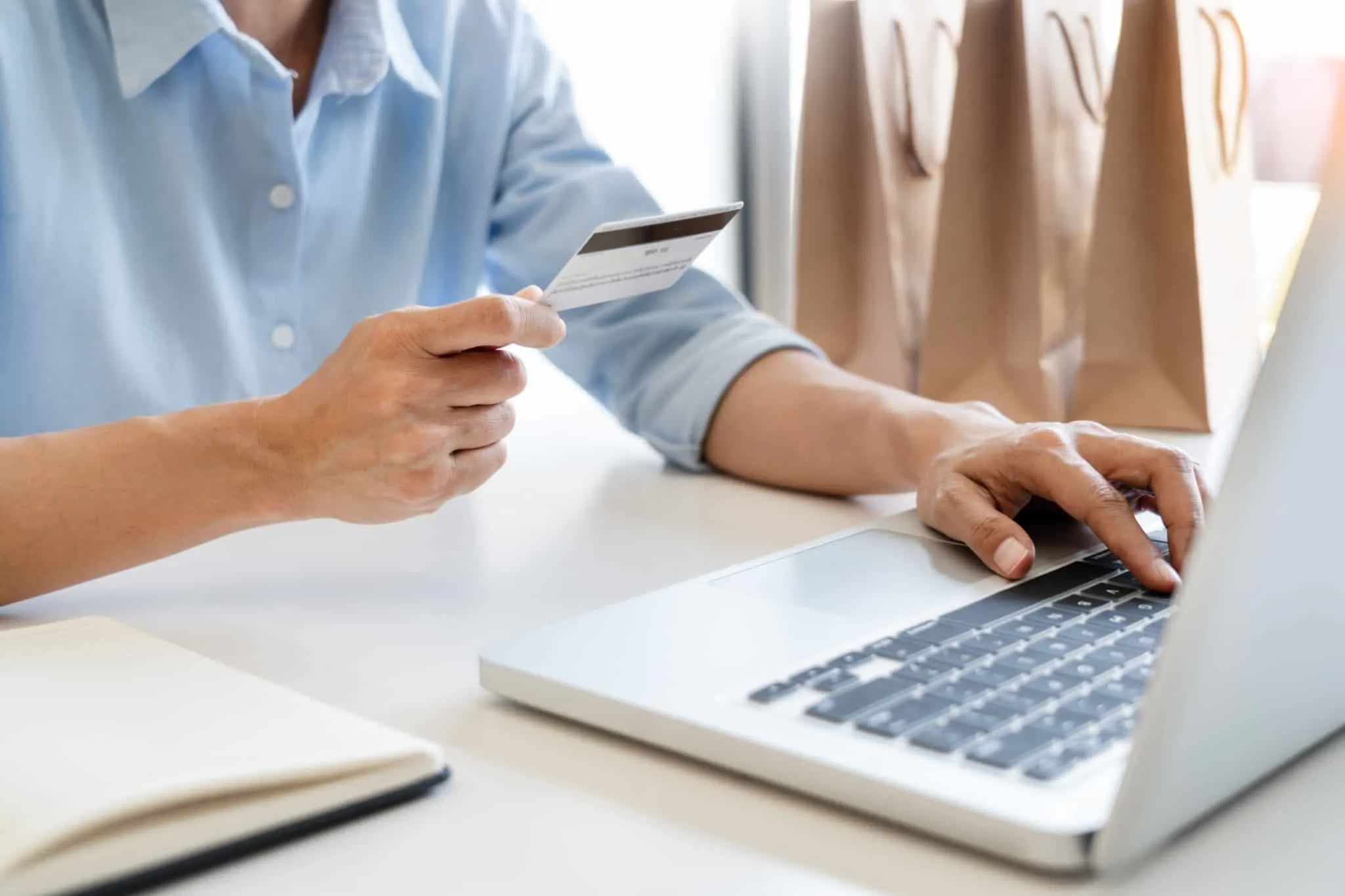 O que são as siglas CVV ou CVC no cartão de débito e de crédito? homem a fazer compras online a utilizar um cartao branco
