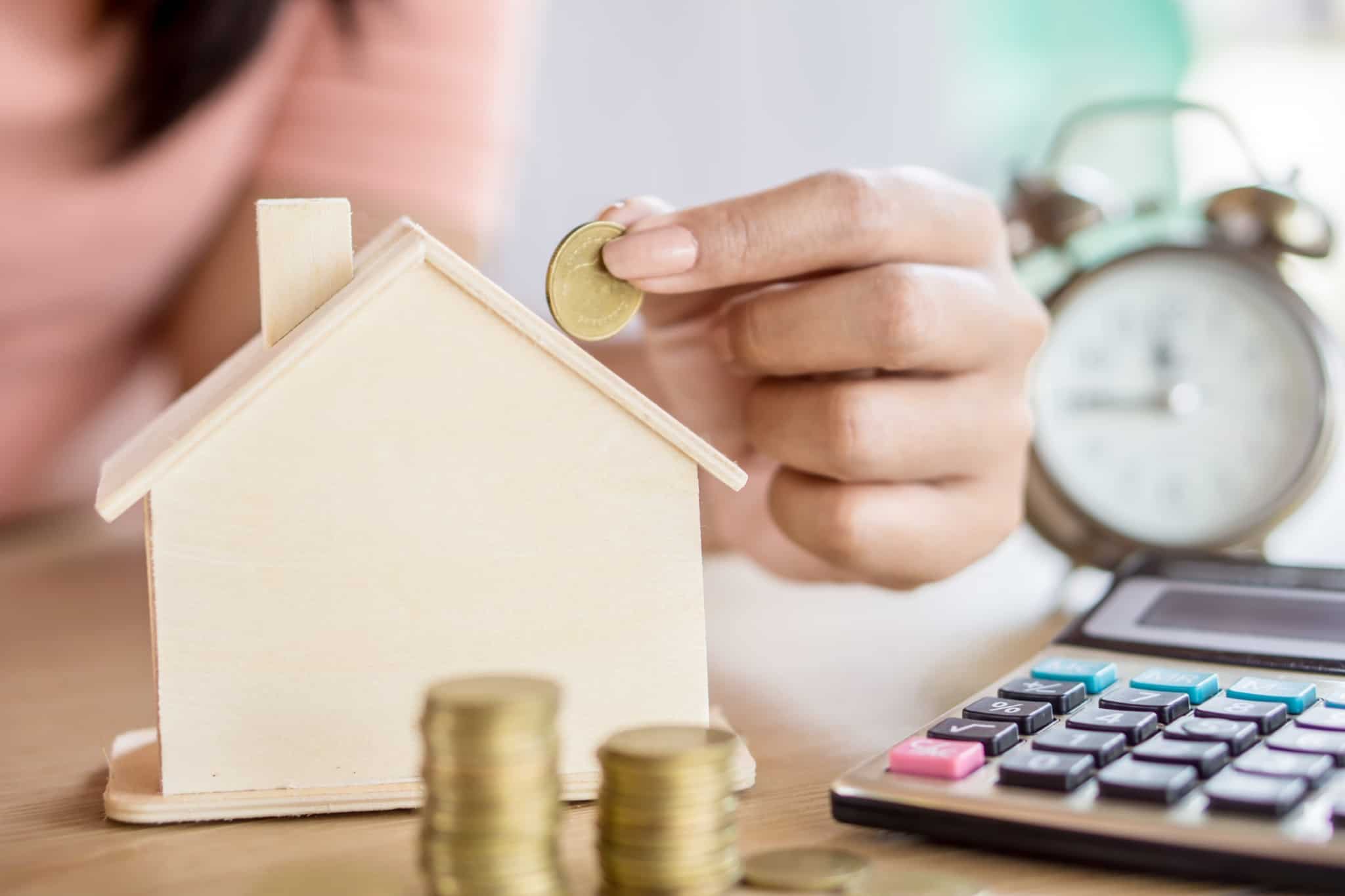 pessoa a colocar moedas num mealheiro em forma de casa