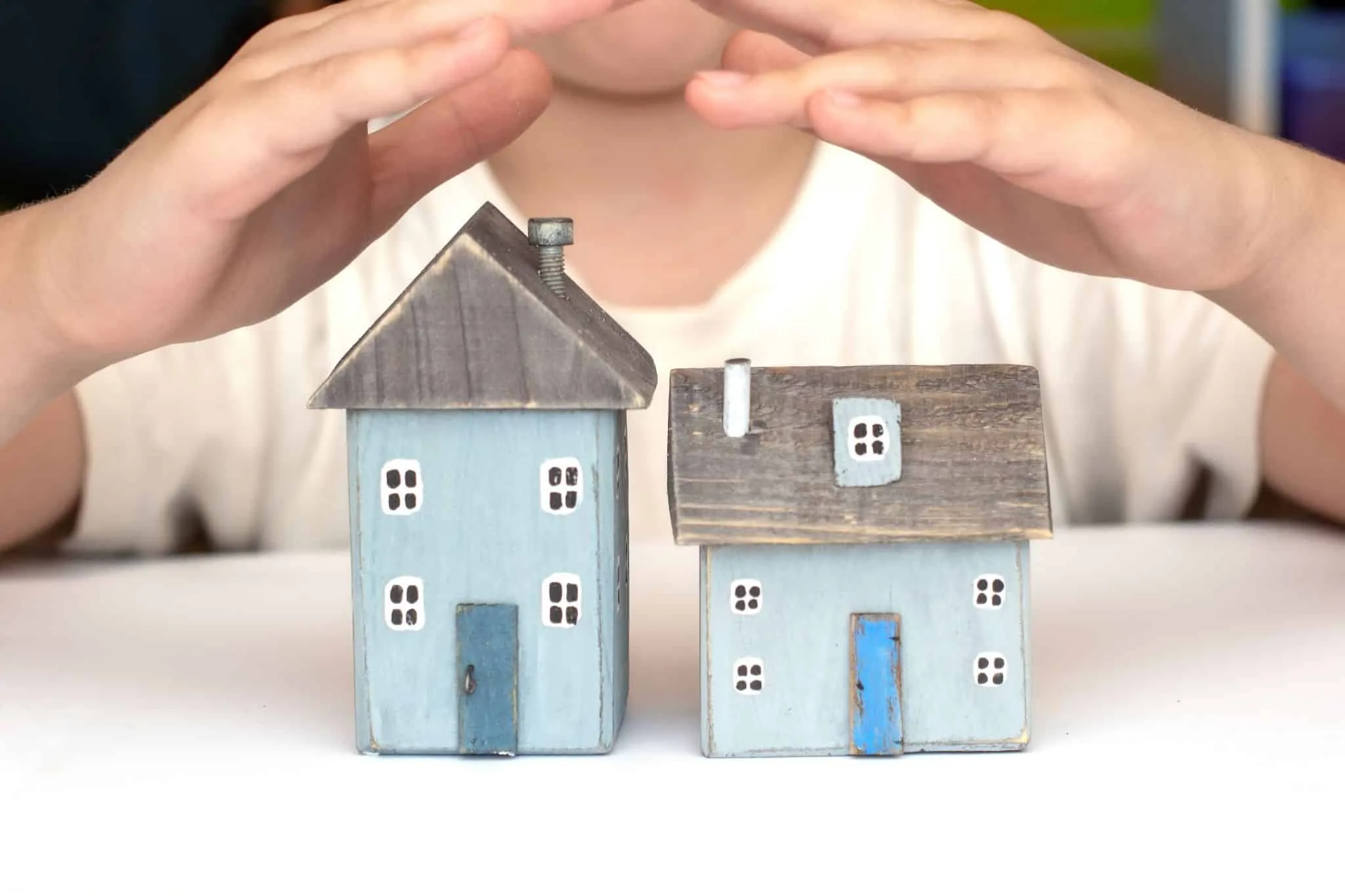 Imagem de duas casas em miniatura com duas mãos a proteger
