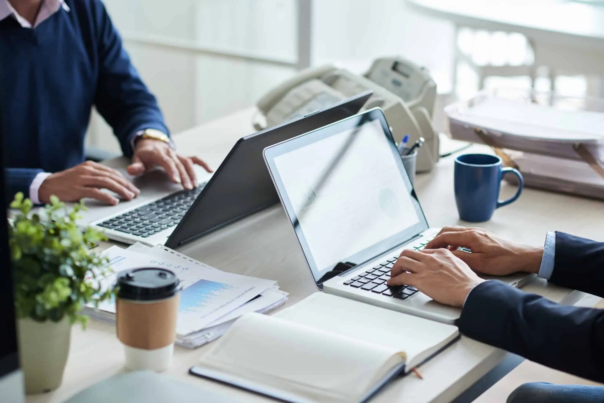 Redução do horário de trabalho: o que é e quais as regras? Duas pessoas trabalham num escritório frente em frente. Cada uma com o seu computador portátil
