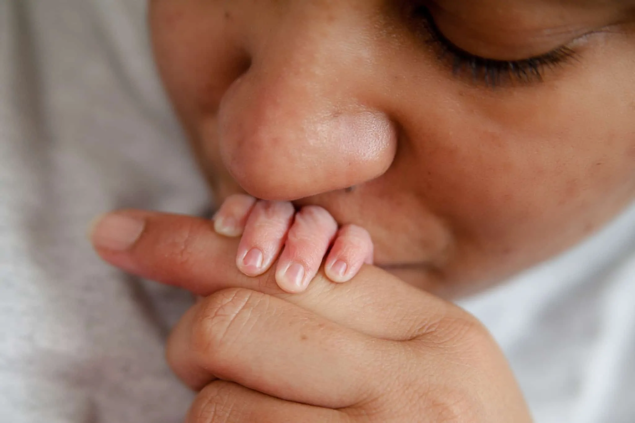 Seguro de saúde para o parto de um filho: o que ter em consideração? Mãe a dar um beijo na mão de um recém-nascido