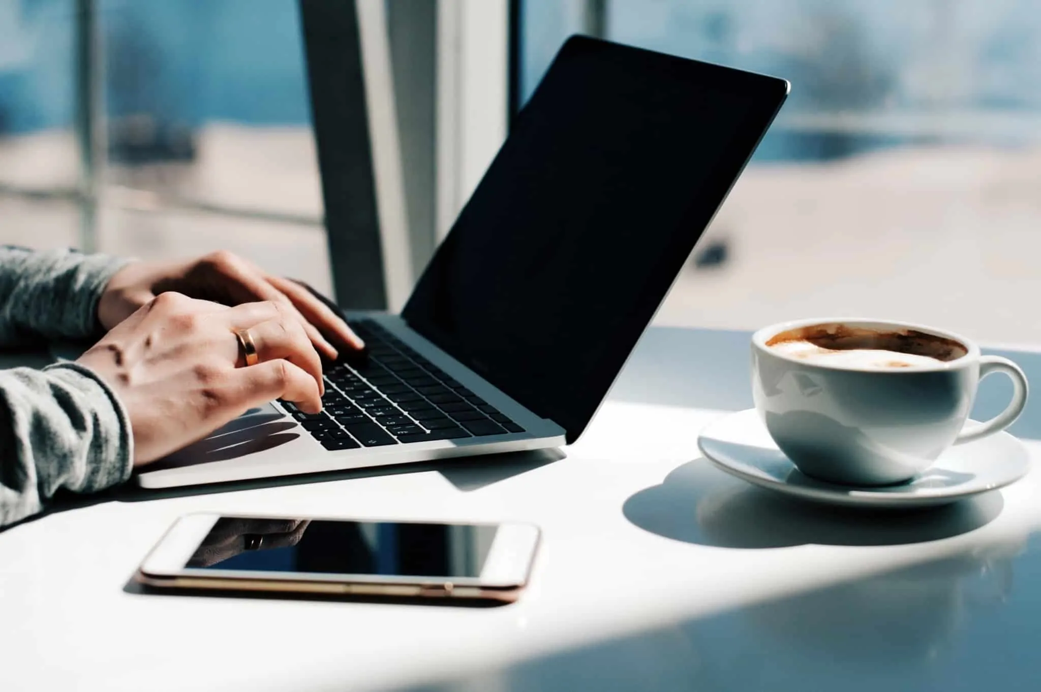 Trabalhador sentado em frente a um computador portátil com o telemóvel e uma chávena de café ao lado