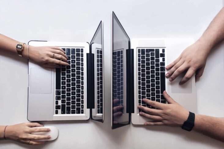 duas pessoas trabalham, frente a frente, em computadores portáteis