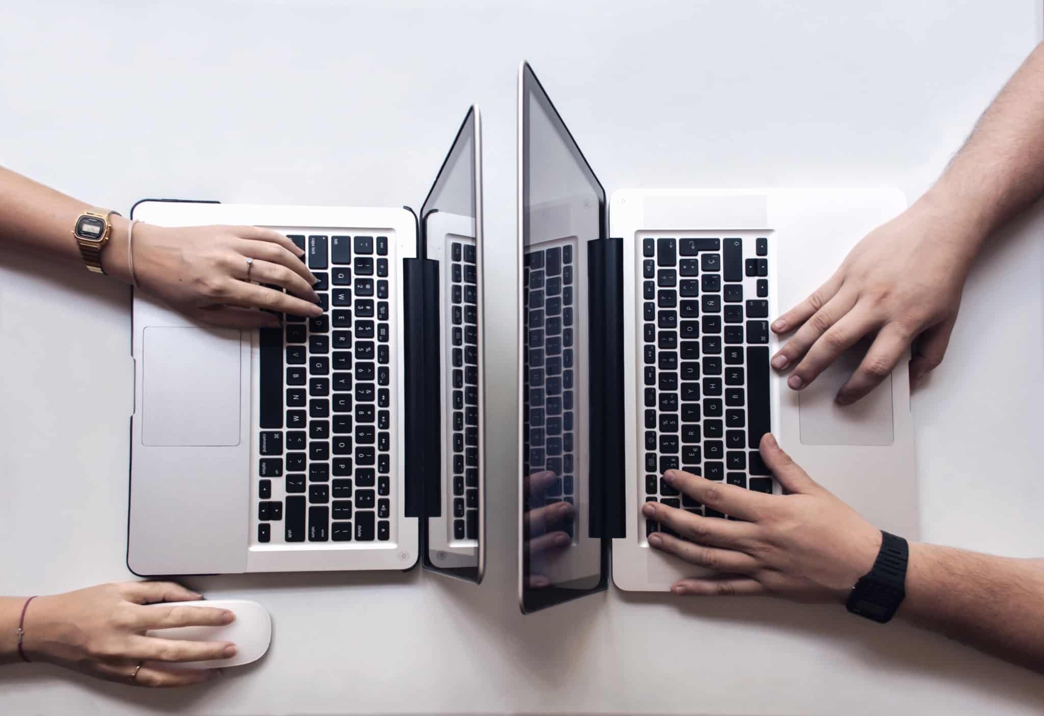 duas pessoas trabalham, frente a frente, em computadores portáteis