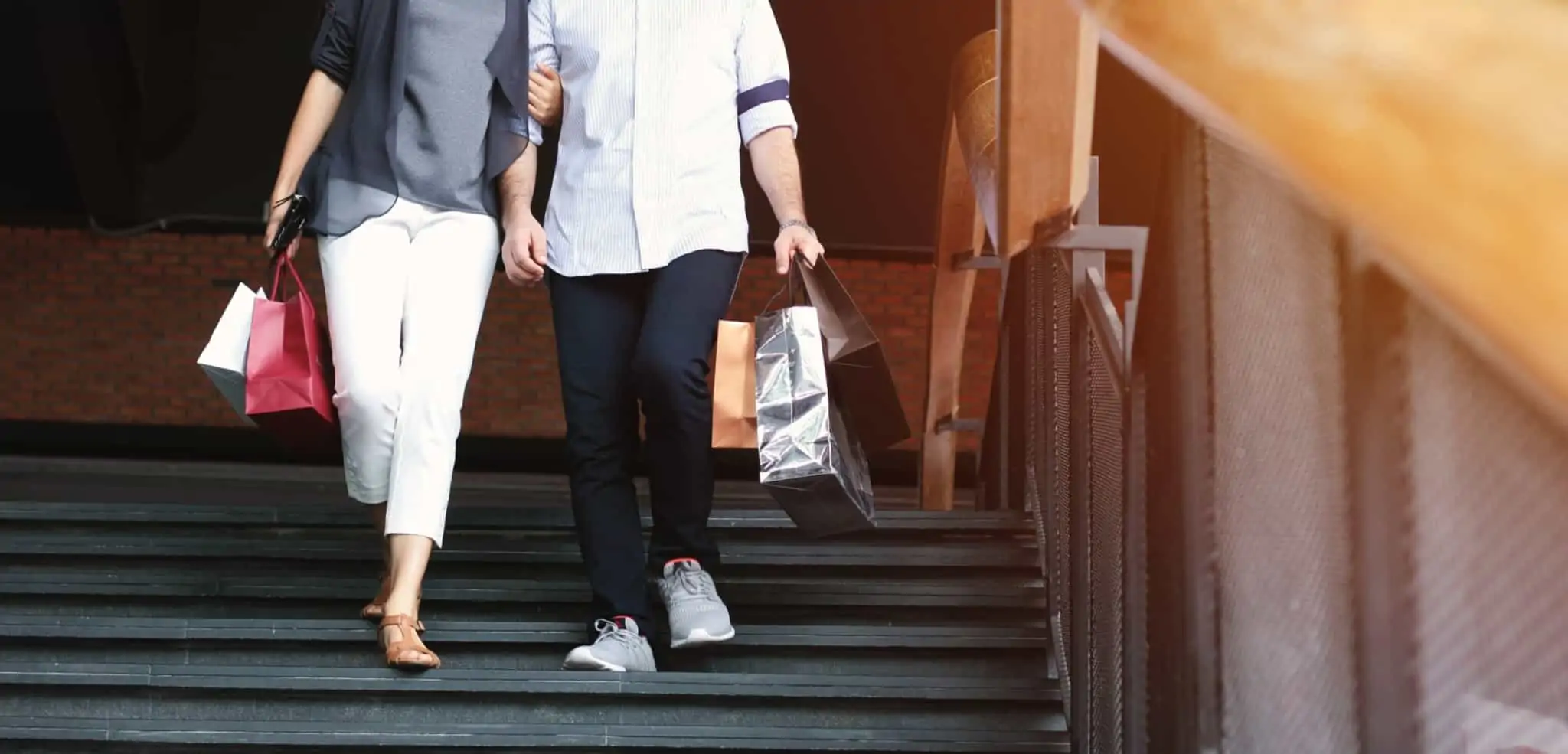 Direitos e deveres dos consumidores: O que estabelece a legislação? Um casal desce uma escadas com sacos de compras nas mãos