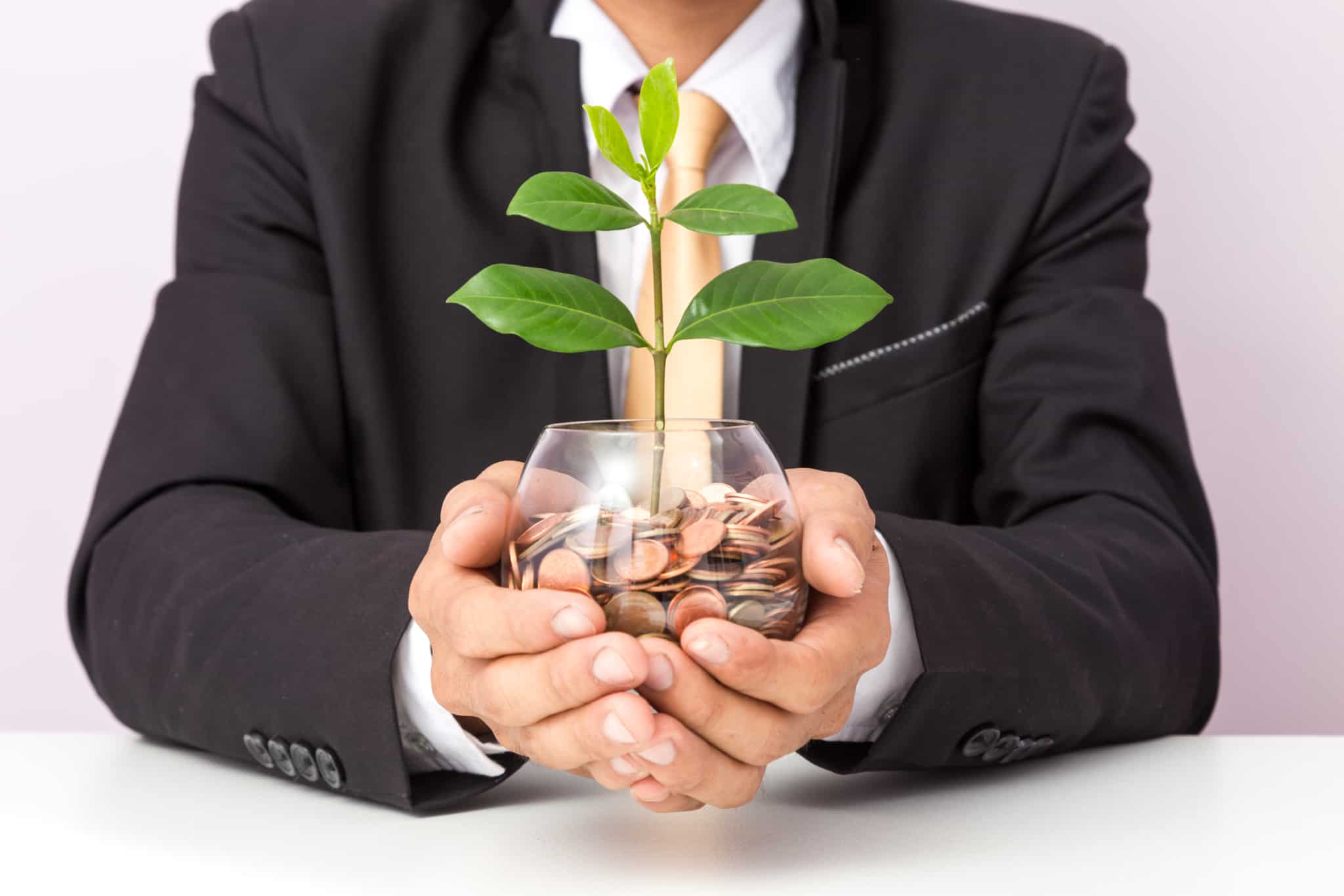 Homem de negócios segura um copo de vidro cheio de moedas, entre as quais está a crescer uma planta
