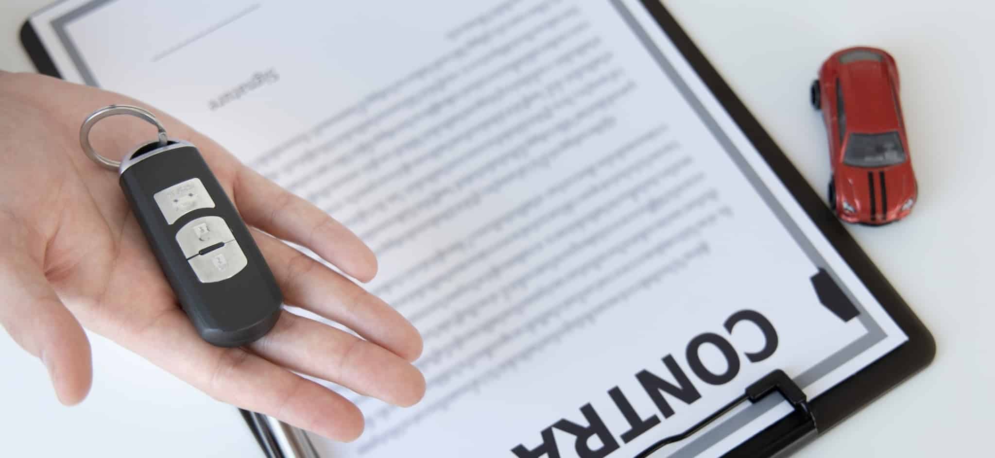 Crédito ao consumo cai quase 23% em 2020 Mão com uma chave de um carro. Por baixo um contrato de crédito automóvel e uma miniatura de carro