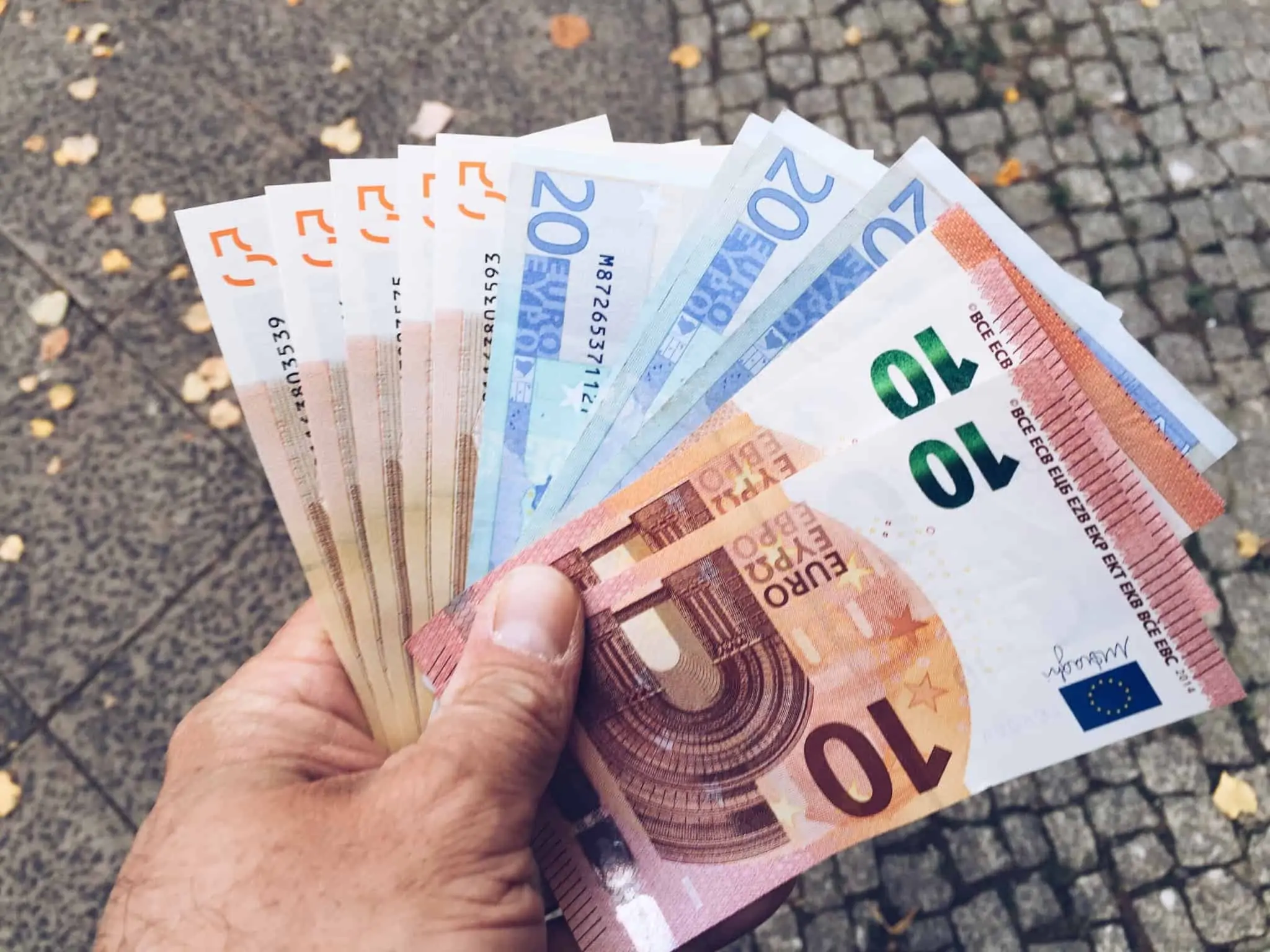 Contrafação de dinheiro: o que fazer com uma nota falsa? Mão de homem a segurar várias notas de euro