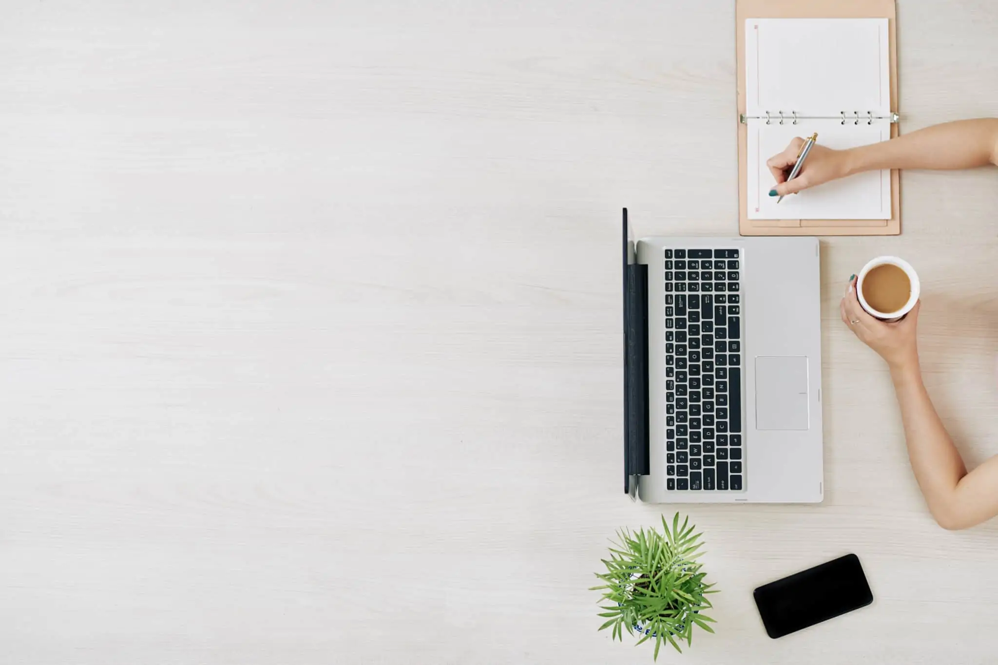 Recibo Verde e Ato Isolado: como emitir? freelancer escreve na sua agenda. À sua frente está o seu portátil e o seu telemóvel