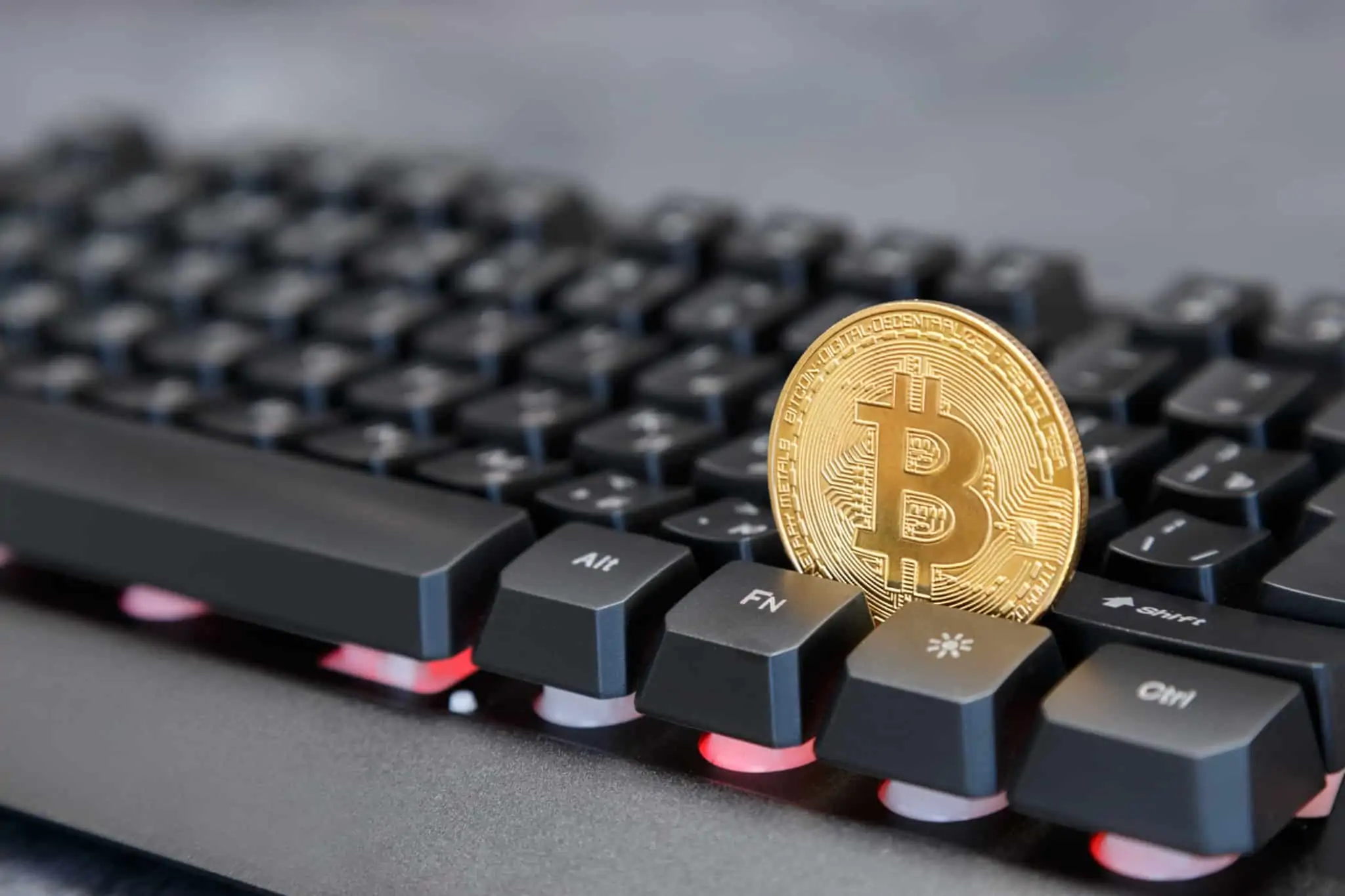 moeda de ouro com o símbolo da bitcoin presa no meio de um teclado de um computador