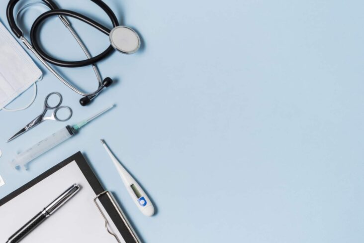 vários instrumentos médicos, como um estetoscópio, uma seringa e um termómetro, em cima de uma mesa