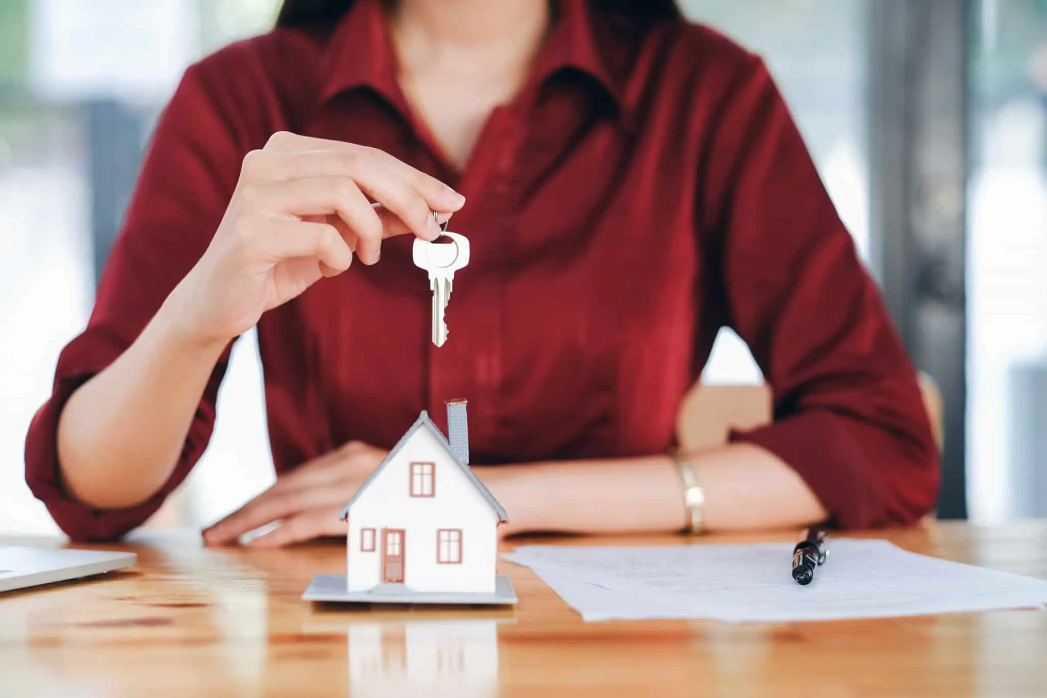 Retoma do contrato de crédito: a chave para não perder a casa numa situação de incumprimento mulher a segurar uma chave da casa com uma casinha de madeira e um contrato