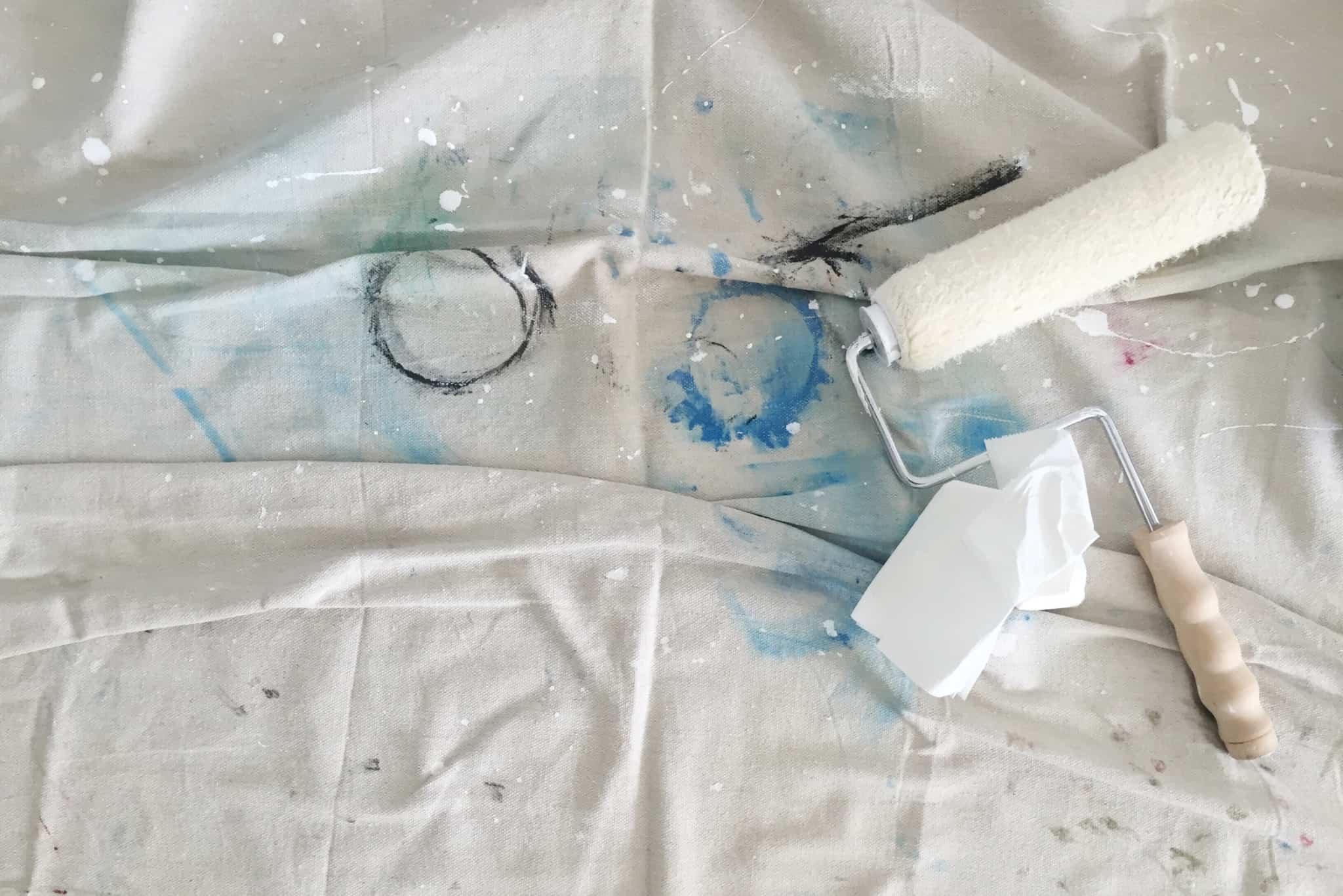 Um rolo de pintura pousado em cima de um lençol branco já sujo com manchas de tinta