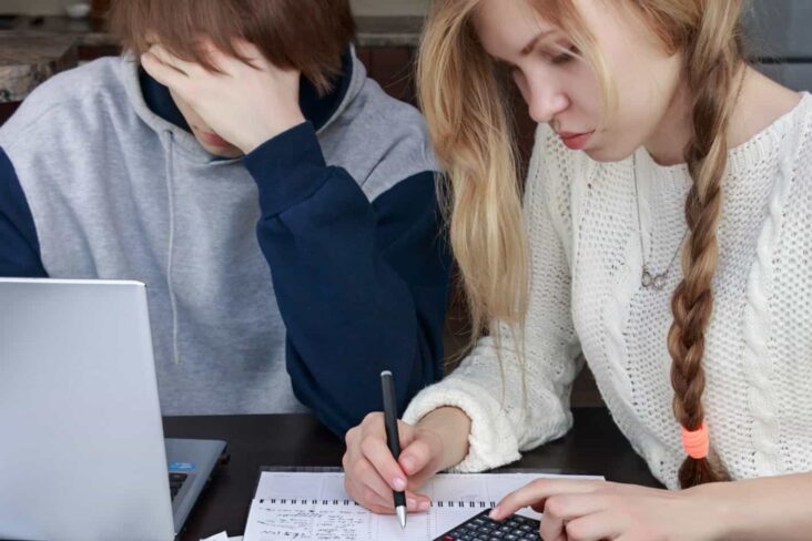 jovem casal faz as contas às suas despesas mensais, consultando documentos, apontando no caderno e usando uma calculadora