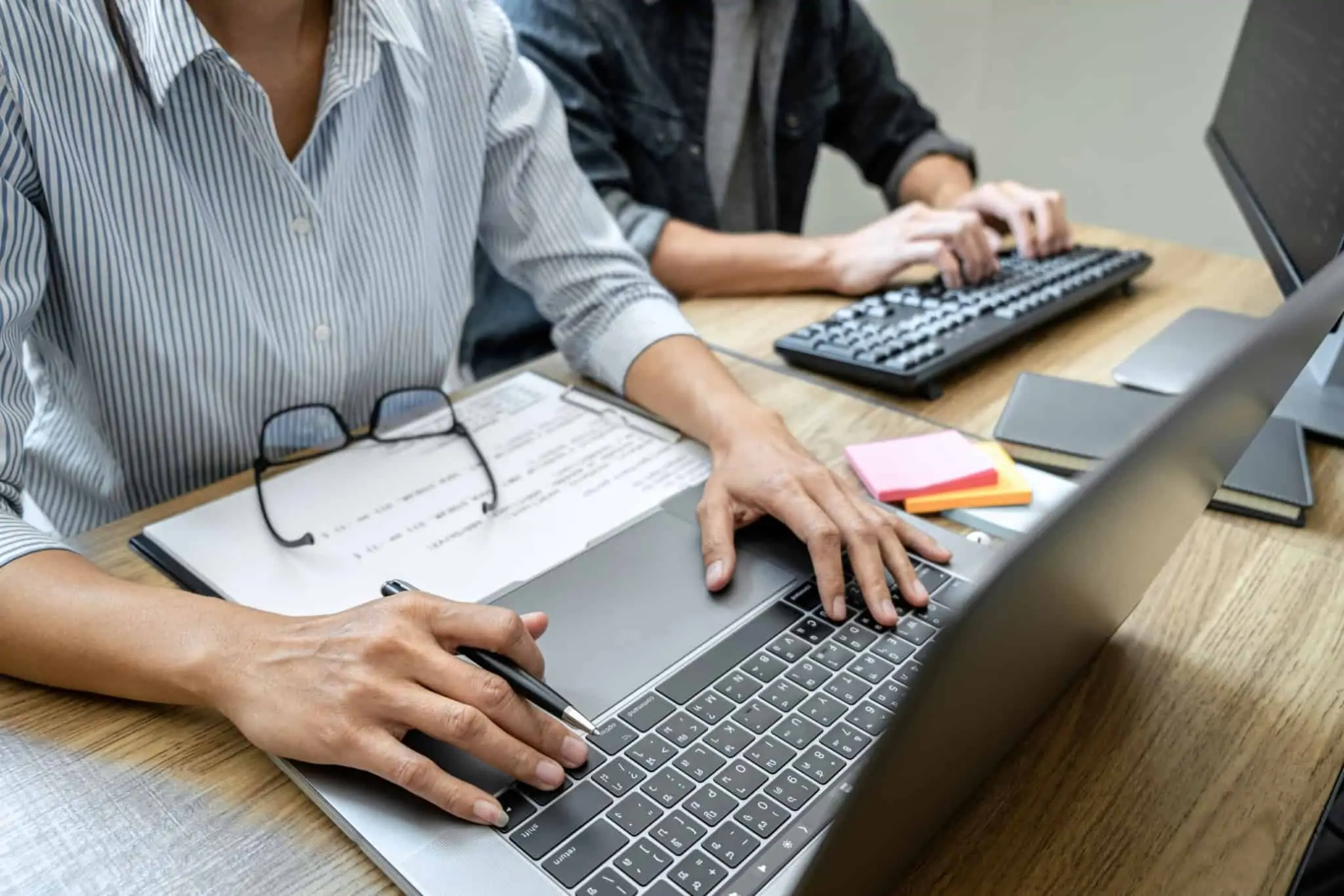 Transferência do local de trabalho: Saiba o que diz a lei Funcionária trabalha ao computador e ao seu lado tem um colega