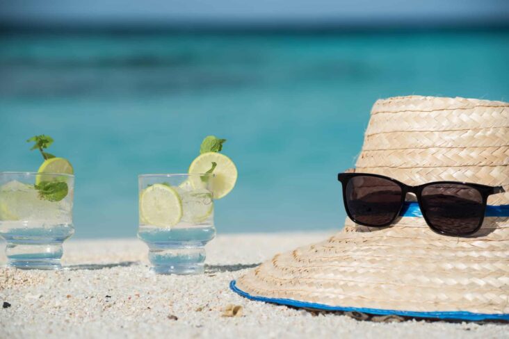 Dois copos com um cocktail pousados à beira da piscina ao lado de um chapéu de sol