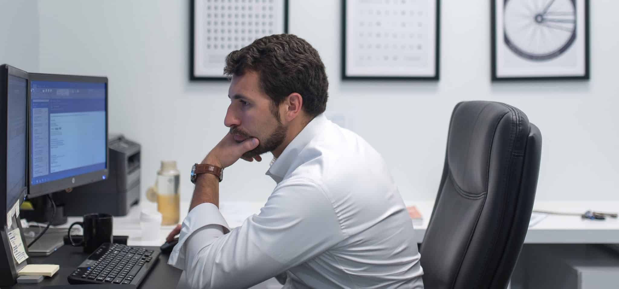 Homem sentado à secretária com a mão no queixo a olhar para o ecrã do computador