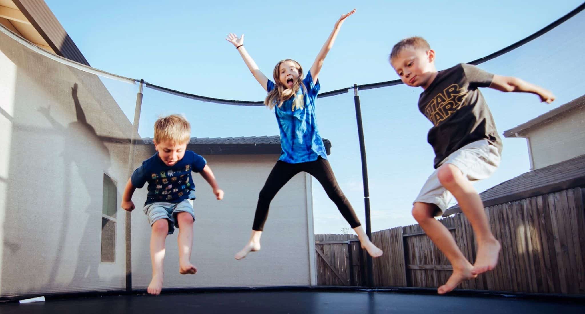 Férias de verão: ideias frescas de atividades para os filhos três crianças saltam num trampolim no quintal