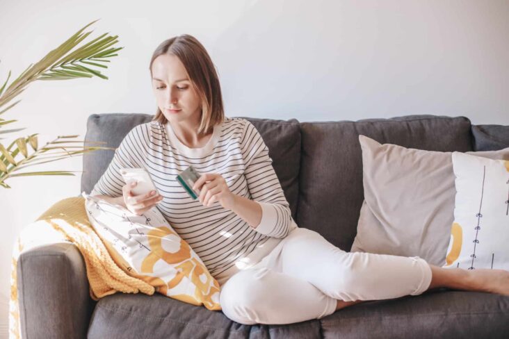 rapariga faz compras online através do seu telemóvel sentada no sofá da sua sala de estar