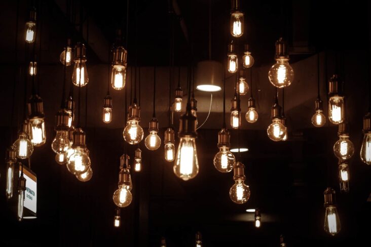 conjunto de candeeiros, de diferentes feitios, acesos e suspensos no teto de uma sala escura