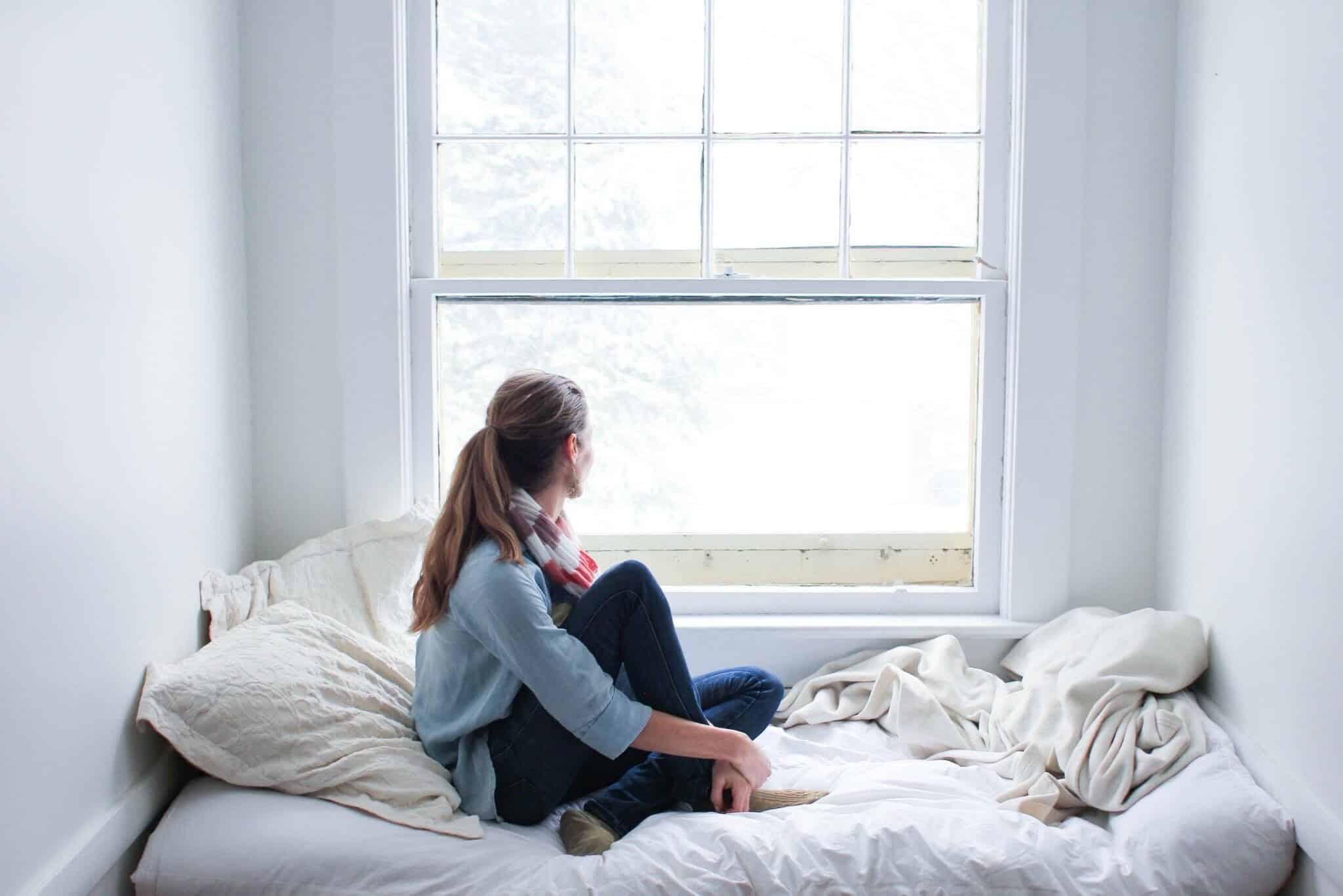 Moratória pública chega ao fim: já sabe quanto vai pagar? Rapariga sentada olha pela janela a evocar o fim da moratória pública