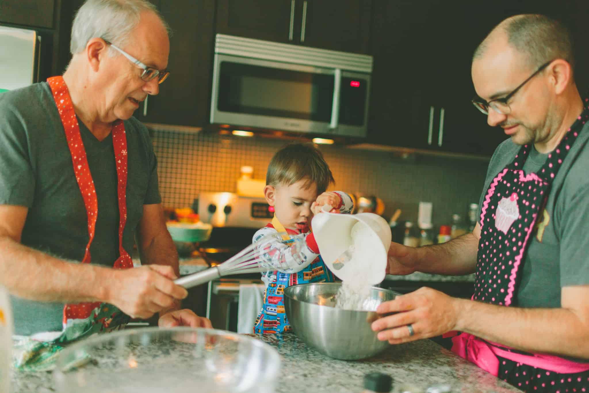 três gerações (avô, filho e neto), juntos na cozinha a partilhar conhecimentos e a criar memórias