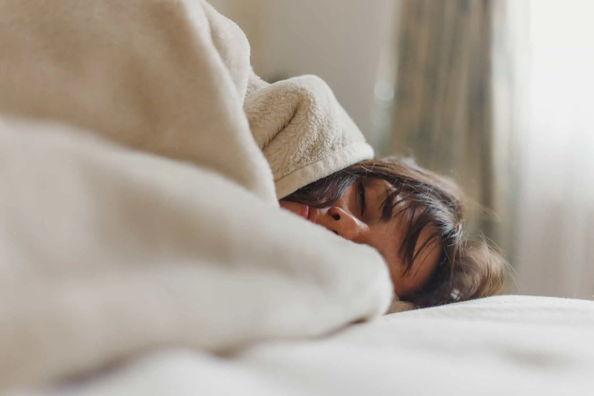 Sabe escolher um colchão? 9 dicas rumo ao conforto total jovem mulher dorme, enroscada em lençóis e manta, com ar muito relax e confortável