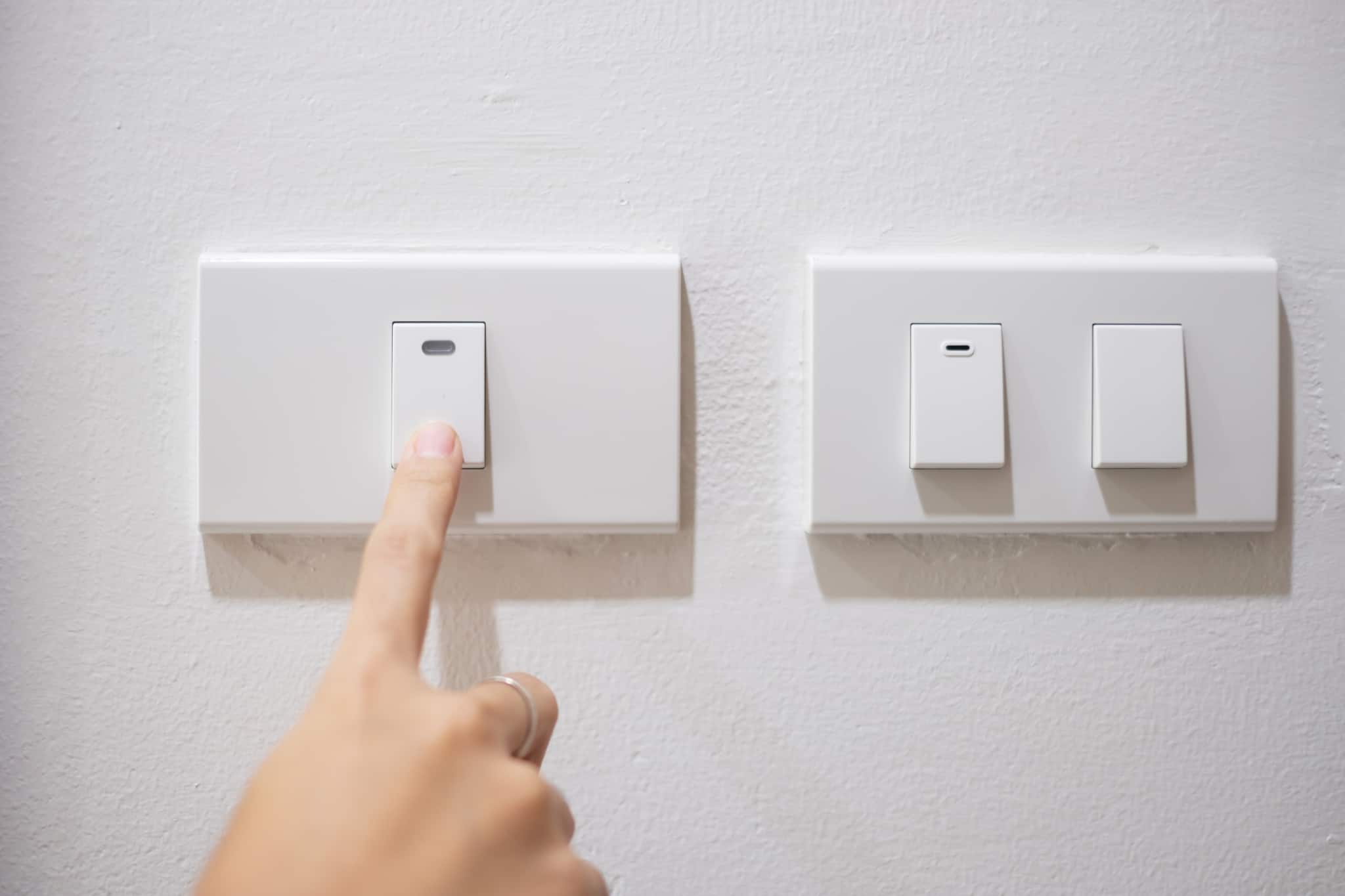 Dedo indicador de uma mão de mulher carrega dum interruptor numa parede de casa