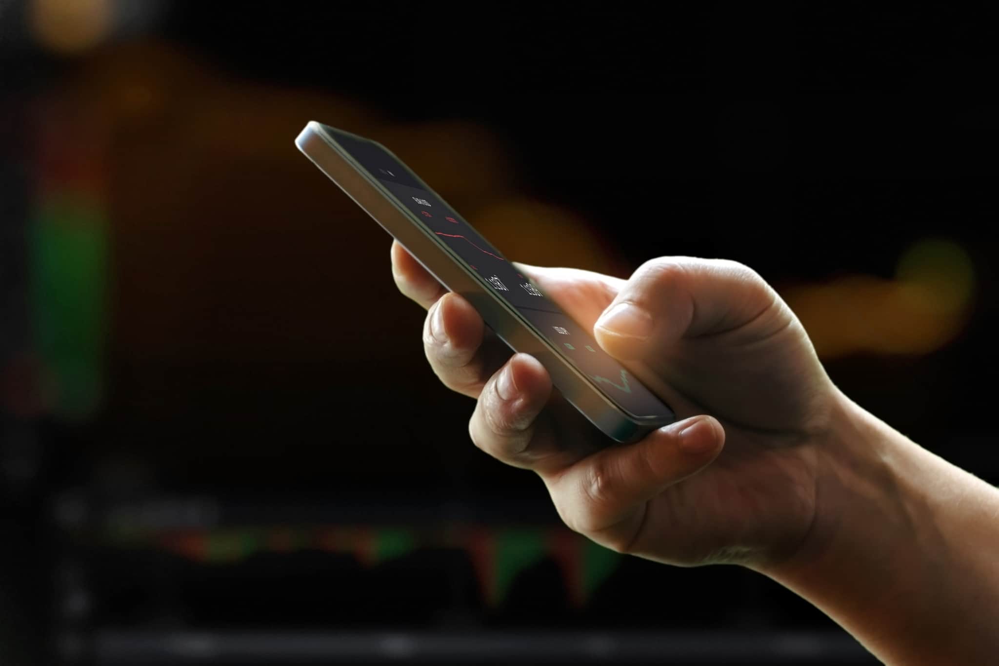 O que são plataformas de investimento peer-to-peer? Mão de homem a segurar o telemóvel, através do qual analisa os seus investimentos realizados através de plataformas peer-to-peer